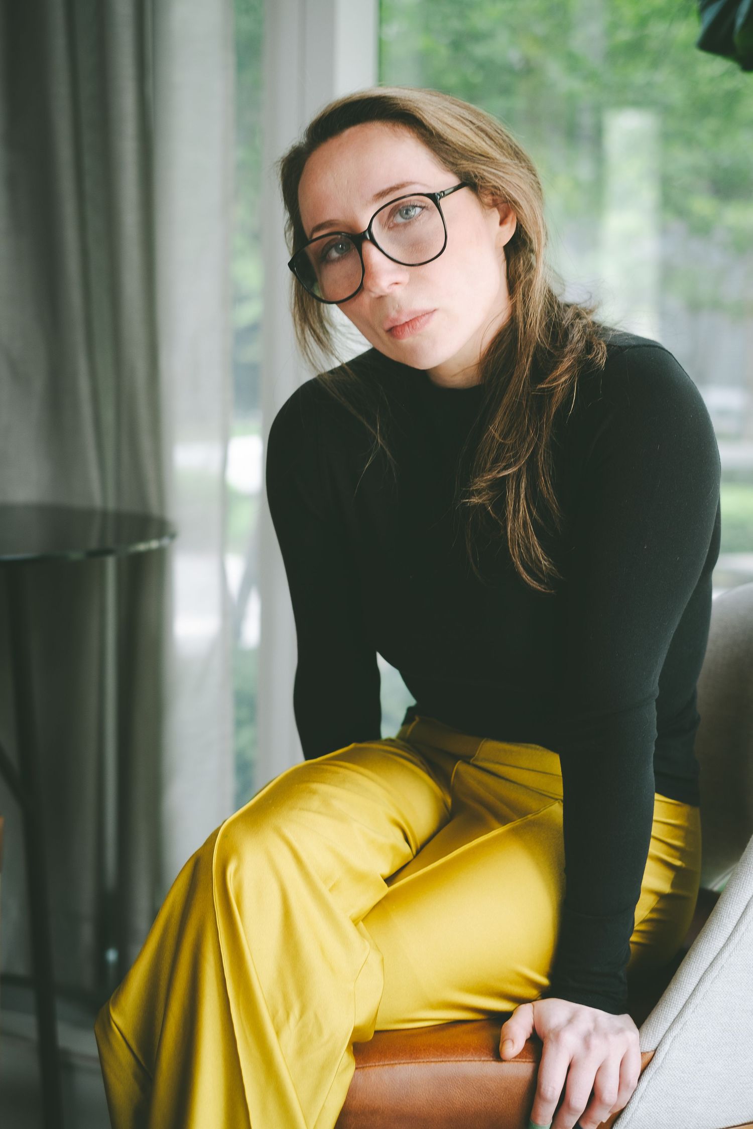 A woman wearing glasses, yellow pants and a black top sitting in a chair