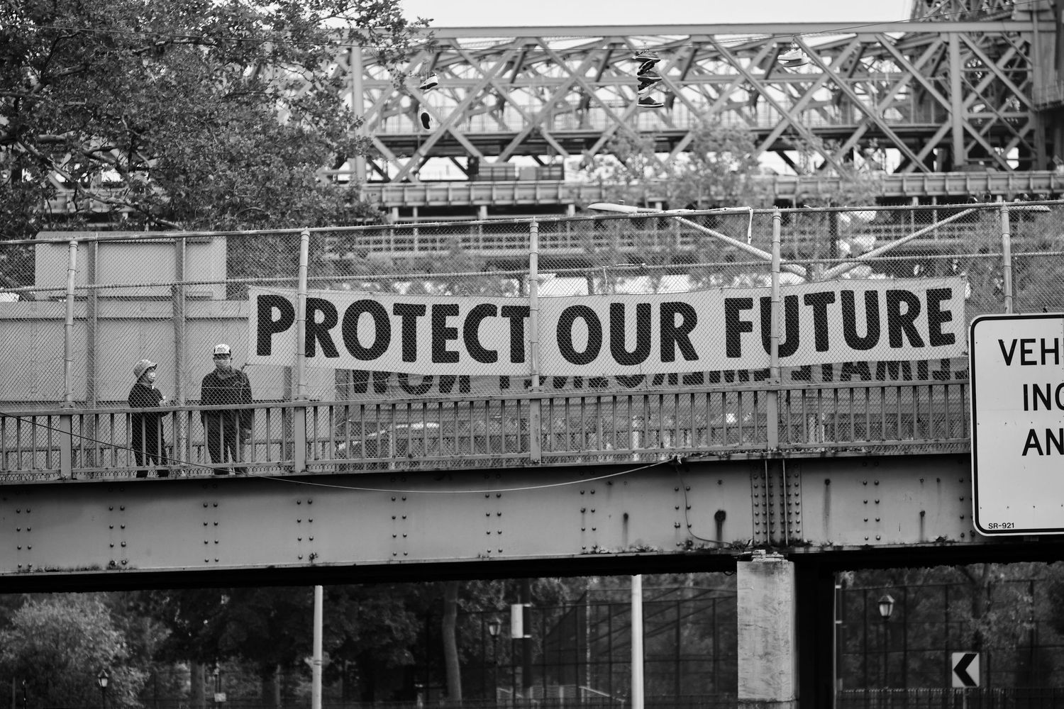 Two people standing on a bridge next to a sign reading 