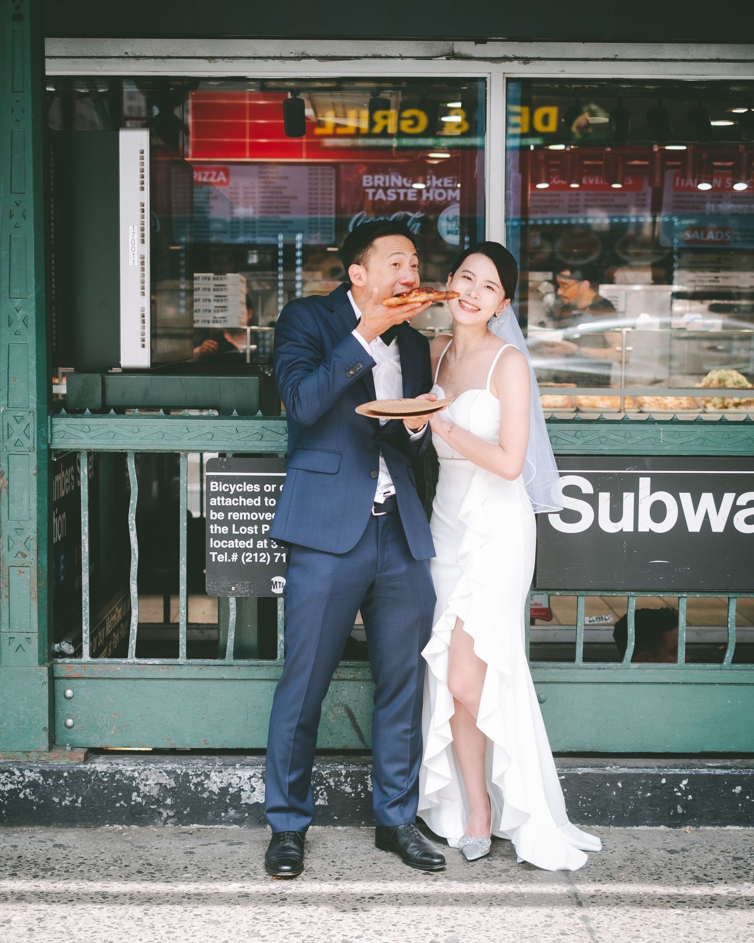 Recently married couple eating pizza in front of a NYC subway entrance