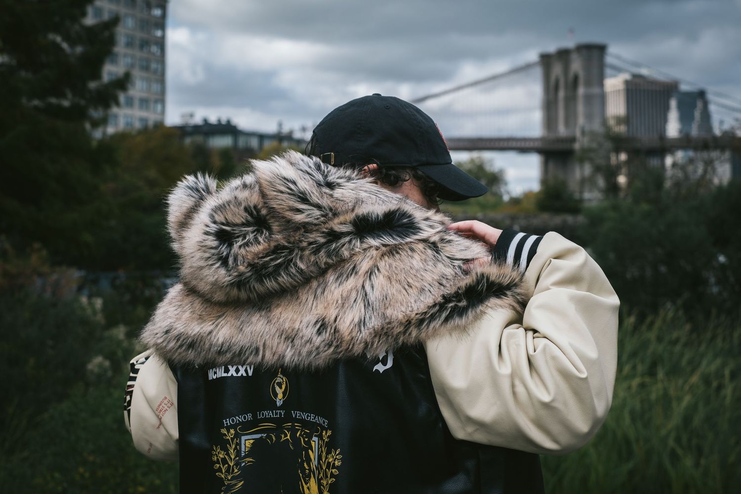 Woman showing the back of her jacket with the Brooklyn Bridge in the background