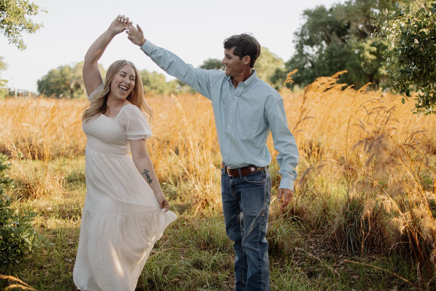 Dancing couple twirls together in a sunlit field with trees in the background.