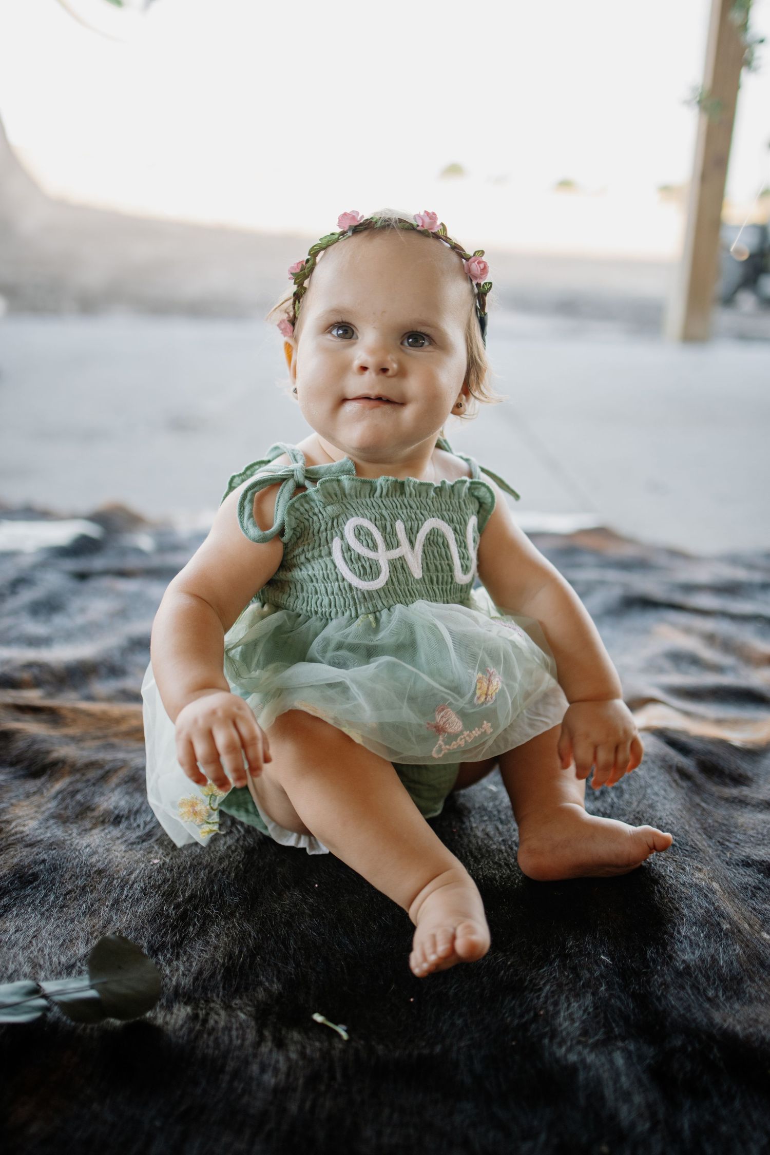 Baby wearing mint green outfit sits on dark blanket during portrait session.