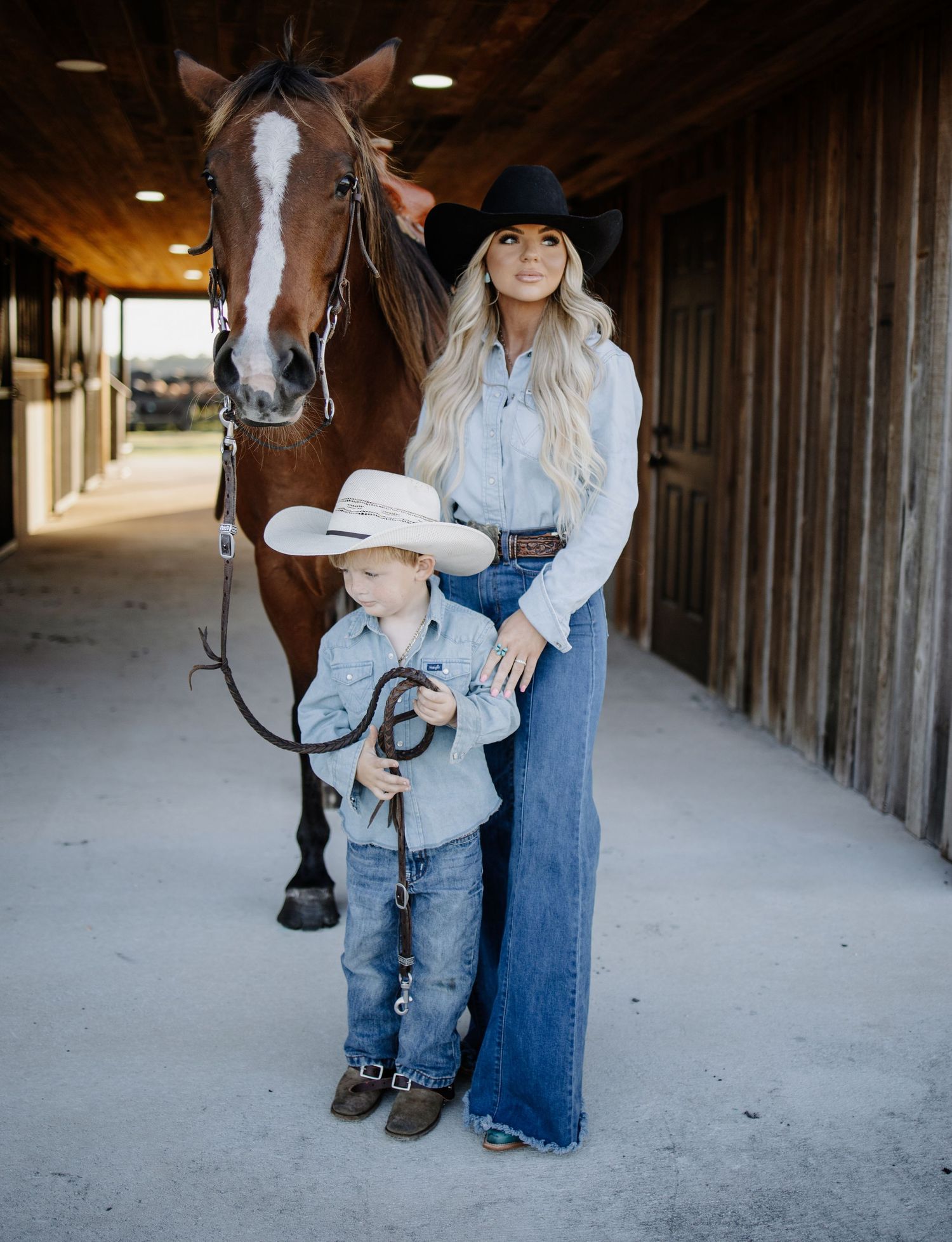 Mother and child interact with horse in rustic stable setting.