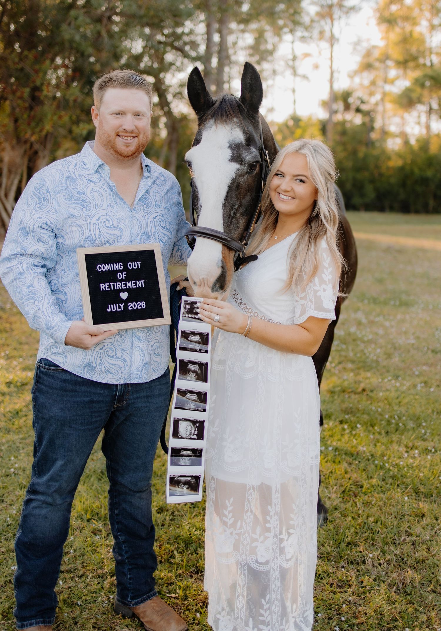 Couple poses with horse while holding pregnancy announcement sign and ultrasound photos.