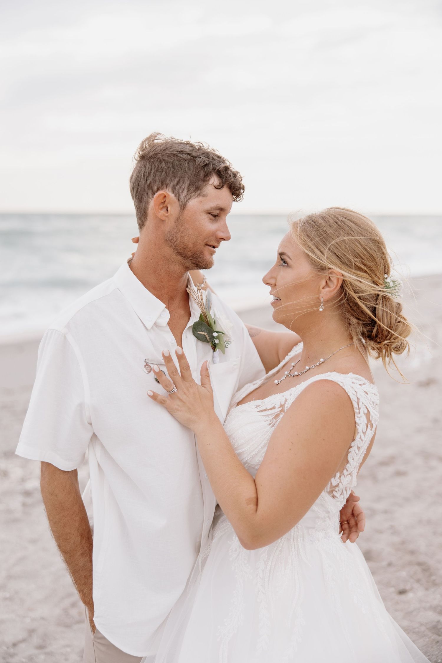 Romantic beach wedding photoshoot with couple in white attire against ocean backdrop.