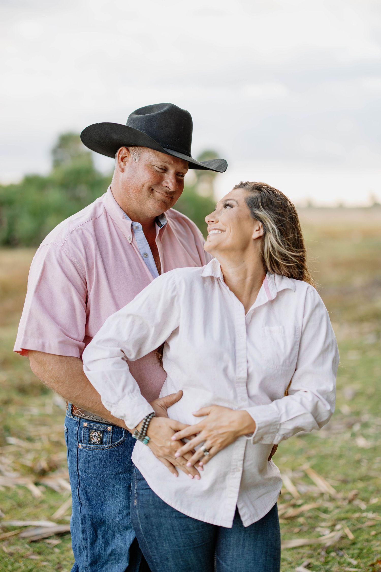 Couple in casual country attire sharing playful moments in an outdoor field.