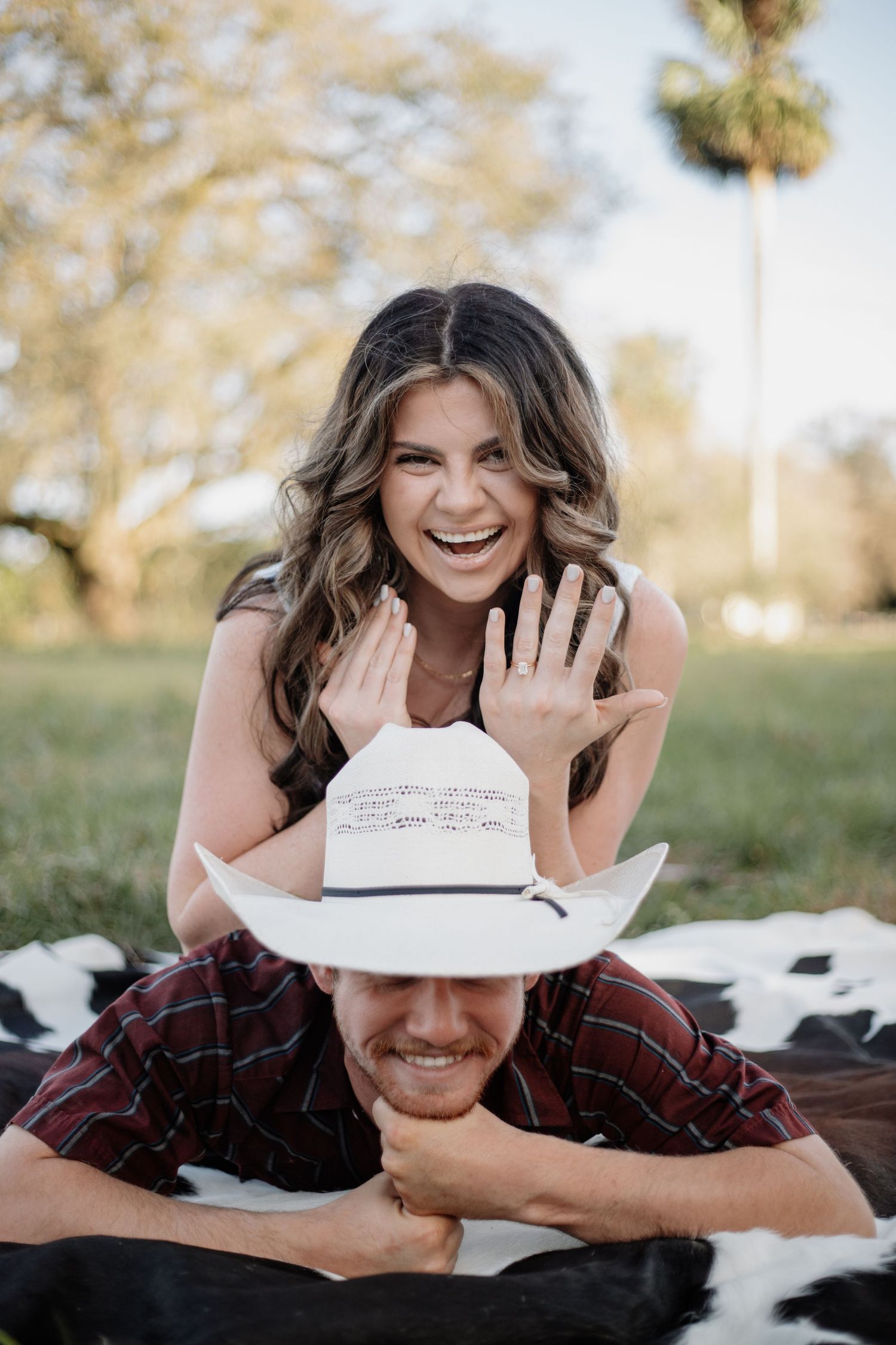 Playful engagement photo with cowboy hat in rustic country setting.