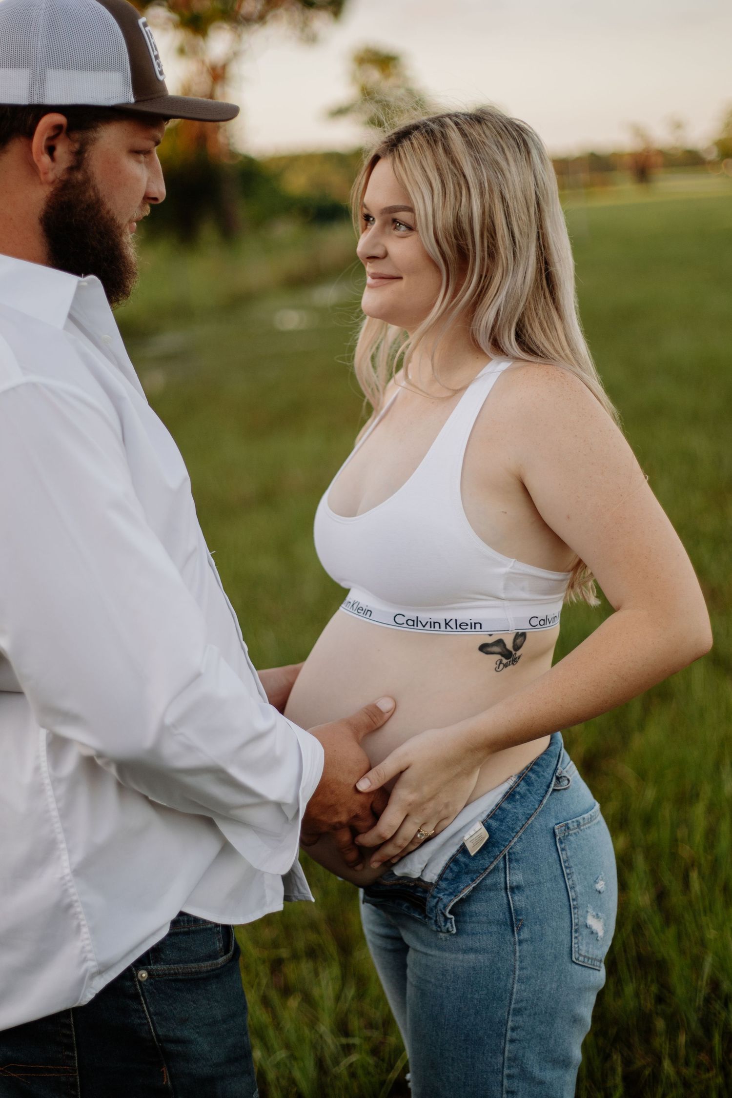 Couple embracing during outdoor maternity photography session at sunset.