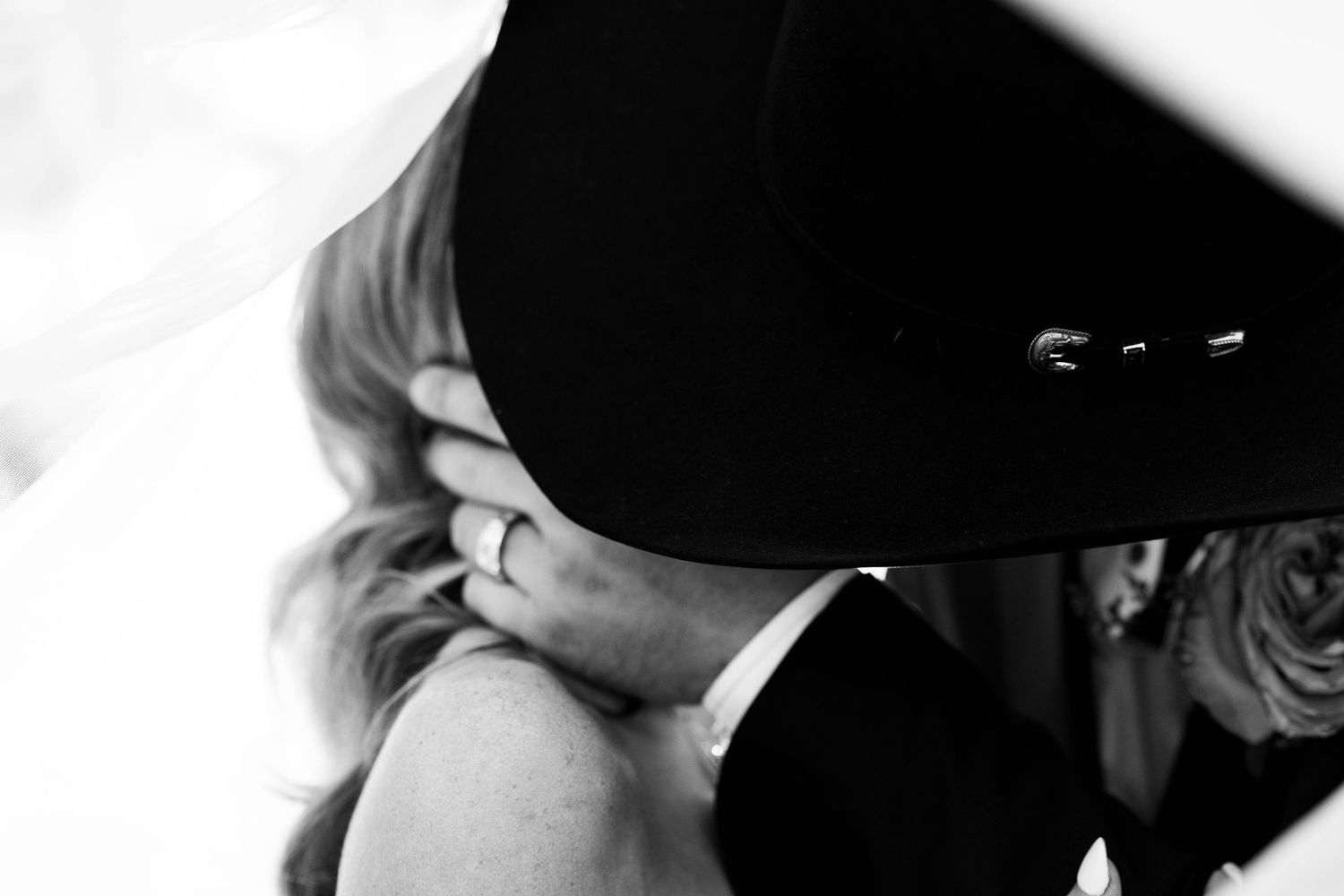 Couple shares intimate moment under black hat in dramatic lighting.