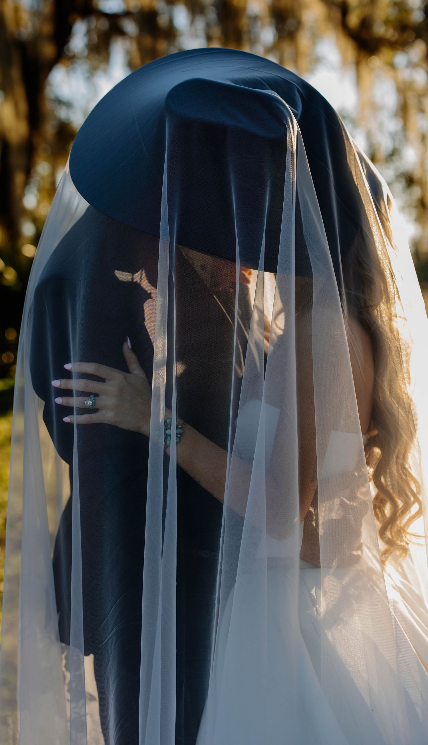 A romantic outdoor photoshoot featuring a couple embracing under a delicate white veil at sunset.