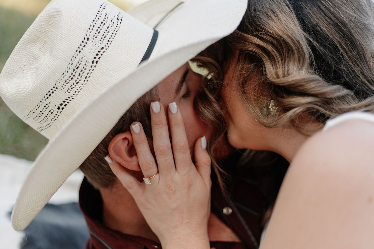 Two people sharing a playful moment under a white cowboy hat.