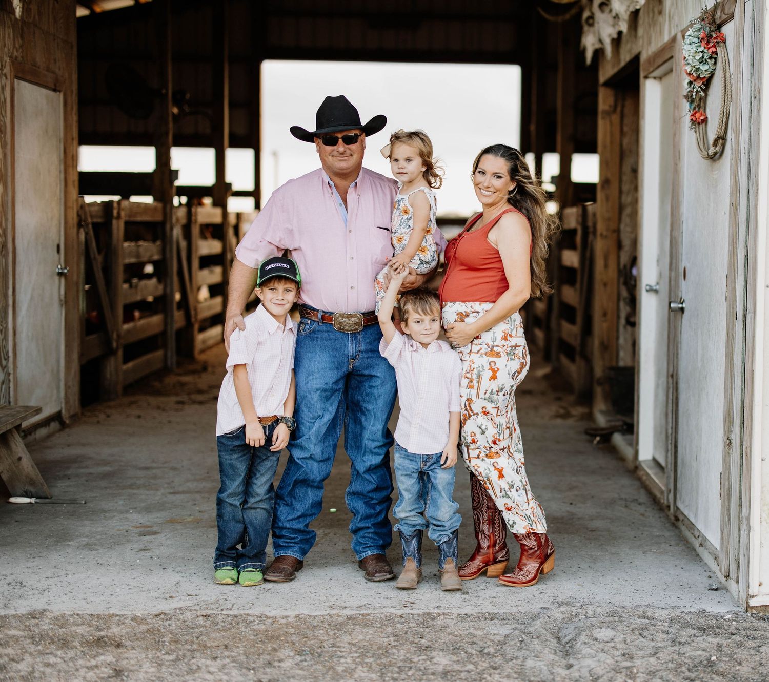 Family in western attire posing together inside a rustic wooden barn.