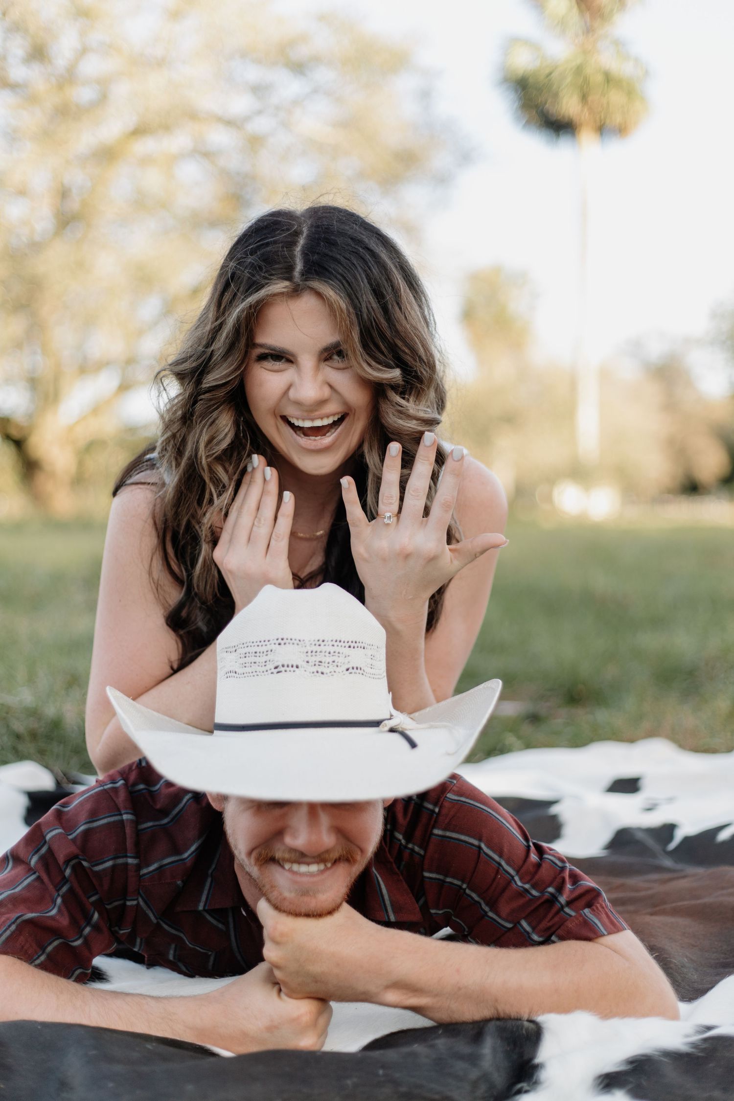 Couple sharing joyful laughter while wearing a white cowboy hat outdoors.