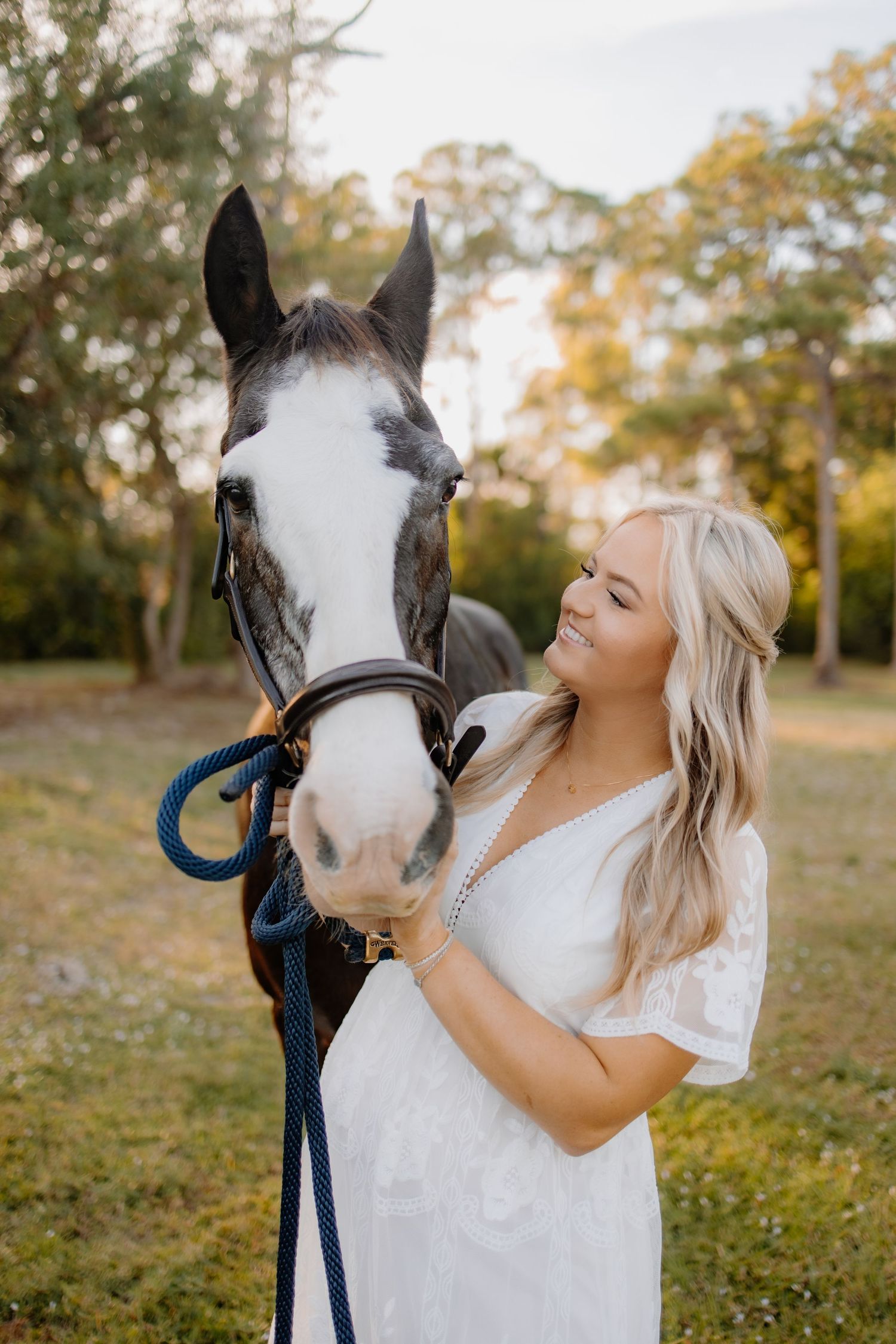 Person in white dress interacting affectionately with a white-faced horse in an autumn field.