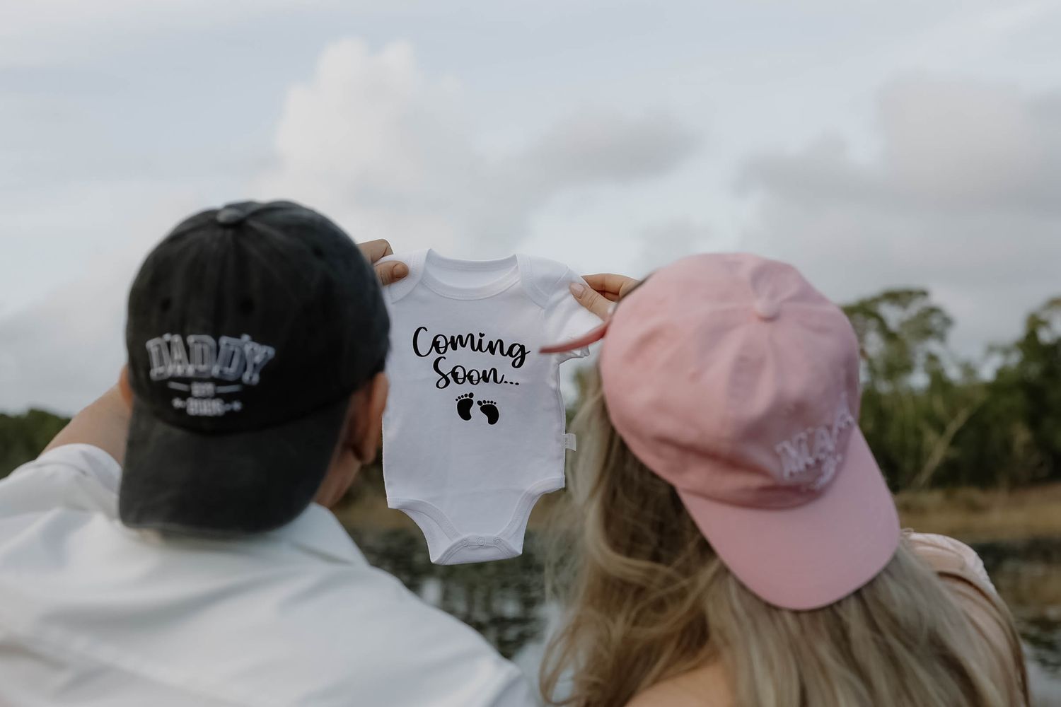 Baby announcement display with onesie and pink hat on rustic background.