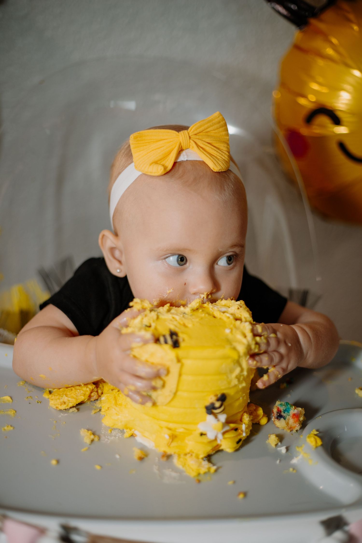 Baby with yellow bow smashing and eating yellow cake during first birthday photoshoot.