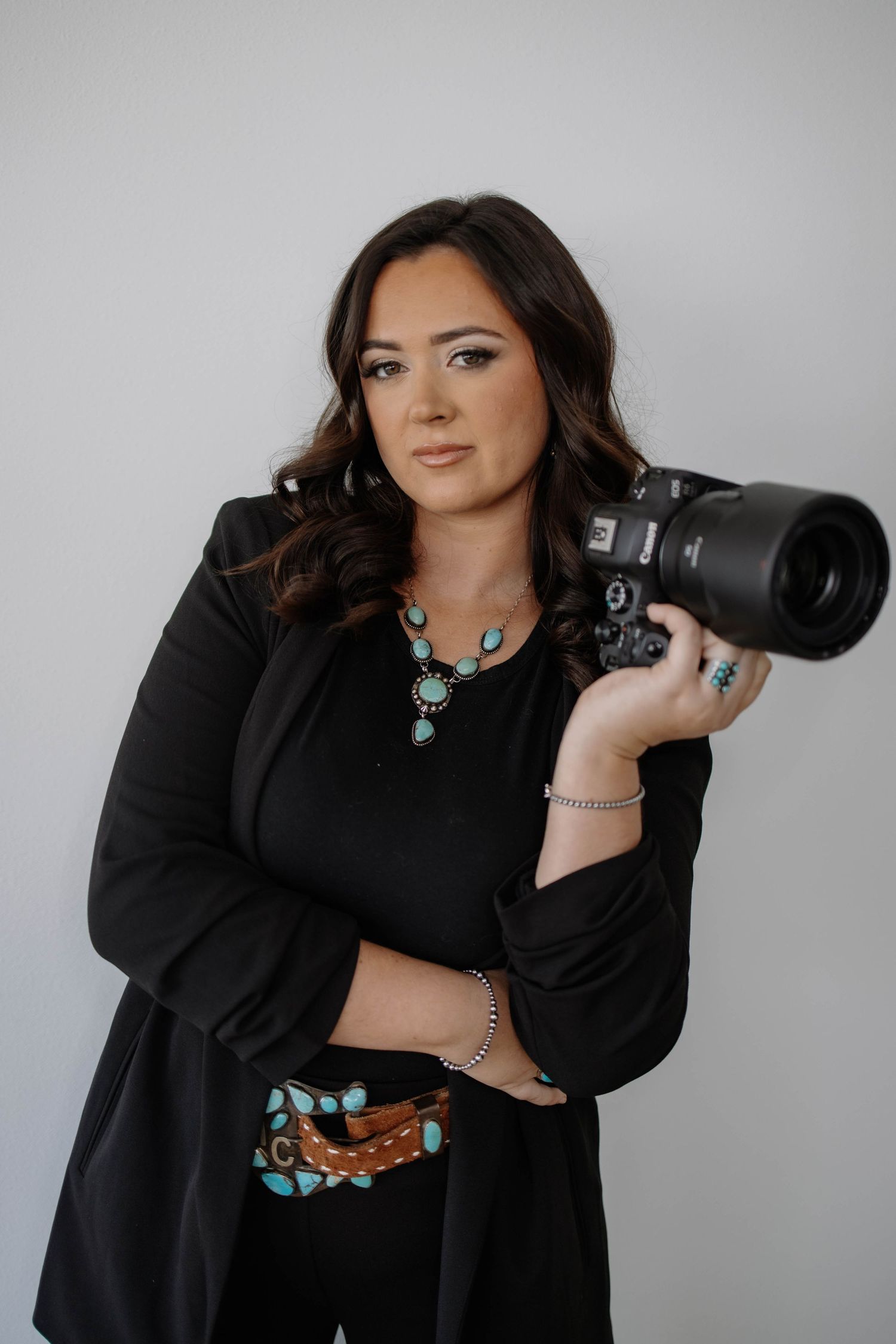 Photographer wearing turquoise jewelry displays camera equipment in studio portraits.