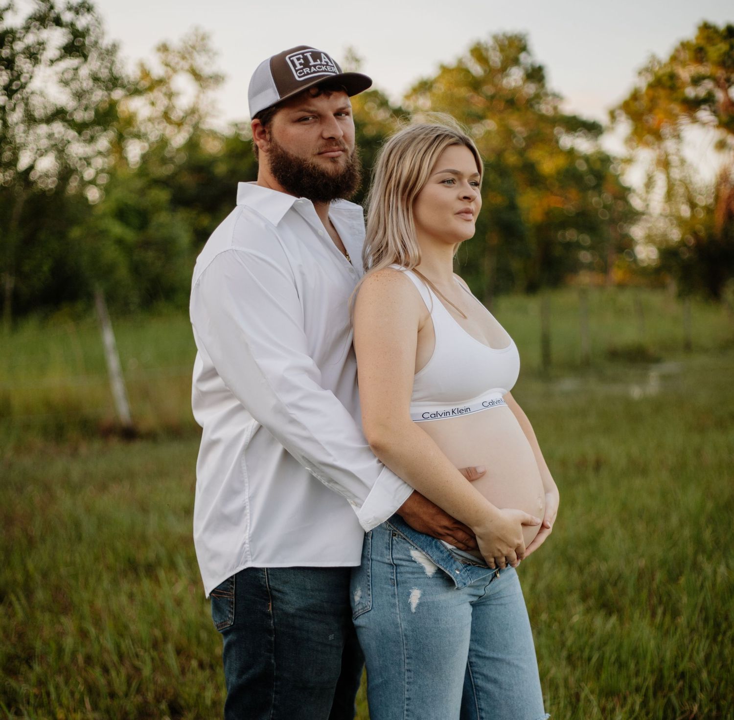 Intimate maternity photoshoot in a sunlit field with casual attire.