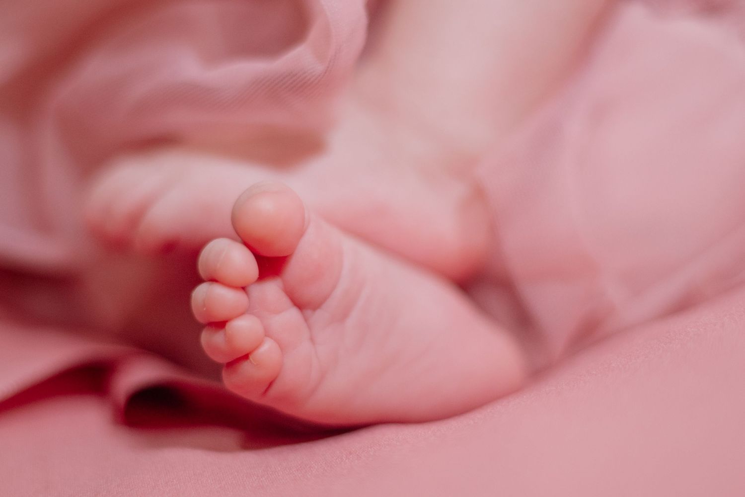 Close-up of tiny newborn feet and toes against soft pink fabric.