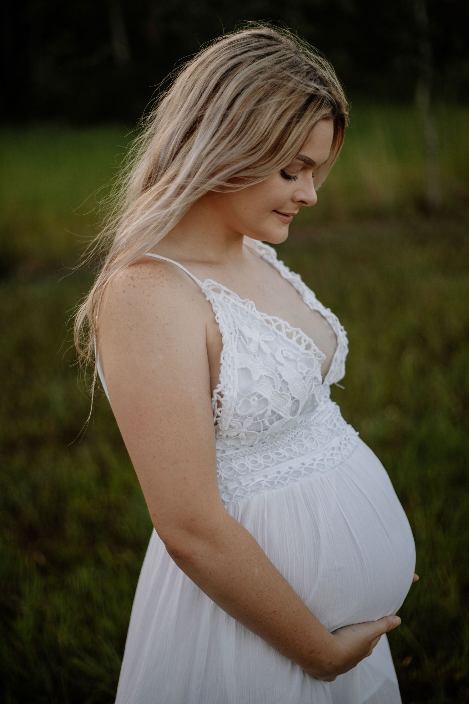 Maternity portrait featuring white lace dress details in natural outdoor setting.