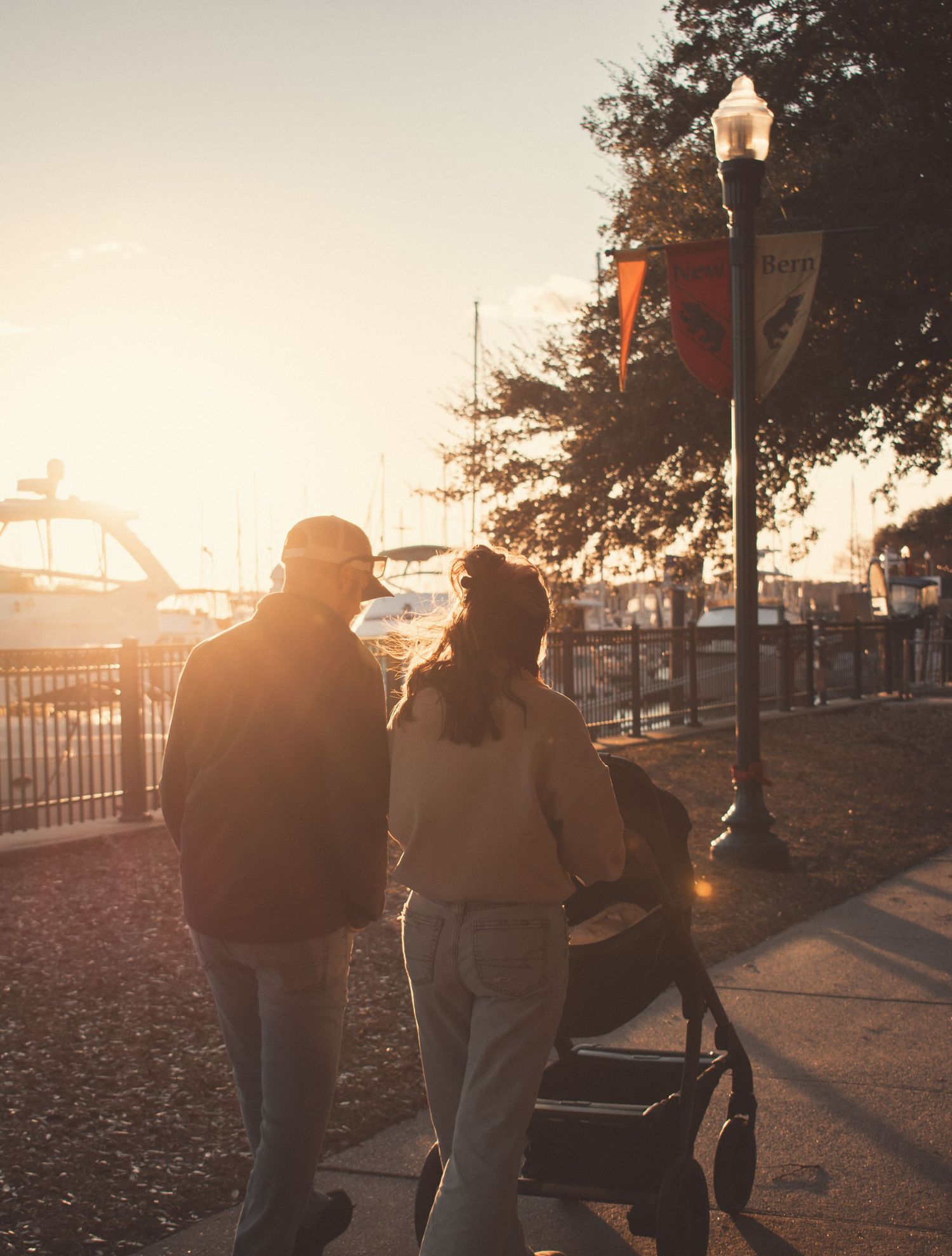 Family strolling at golden hour waterfront promenade with baby stroller at sunset.