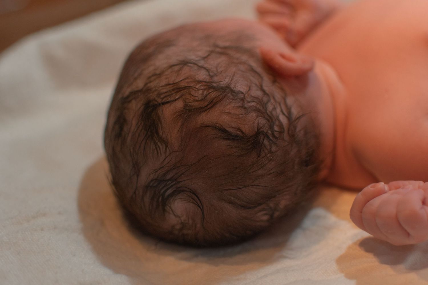 Newborn baby with dark hair lying on white blanket shortly after birth.