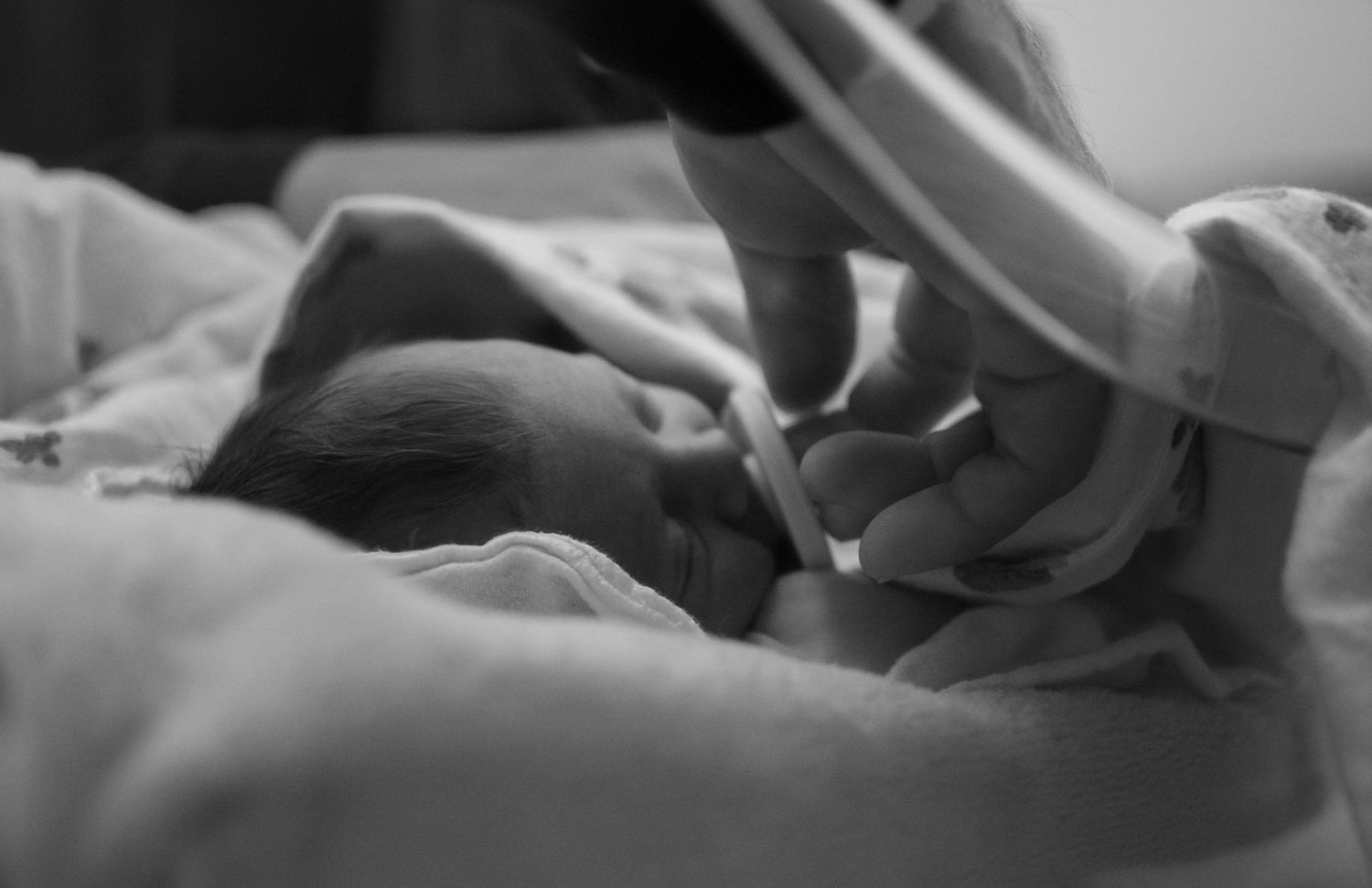 Black and white photo of a newborn baby grasping an adult finger in a hospital bassinet.