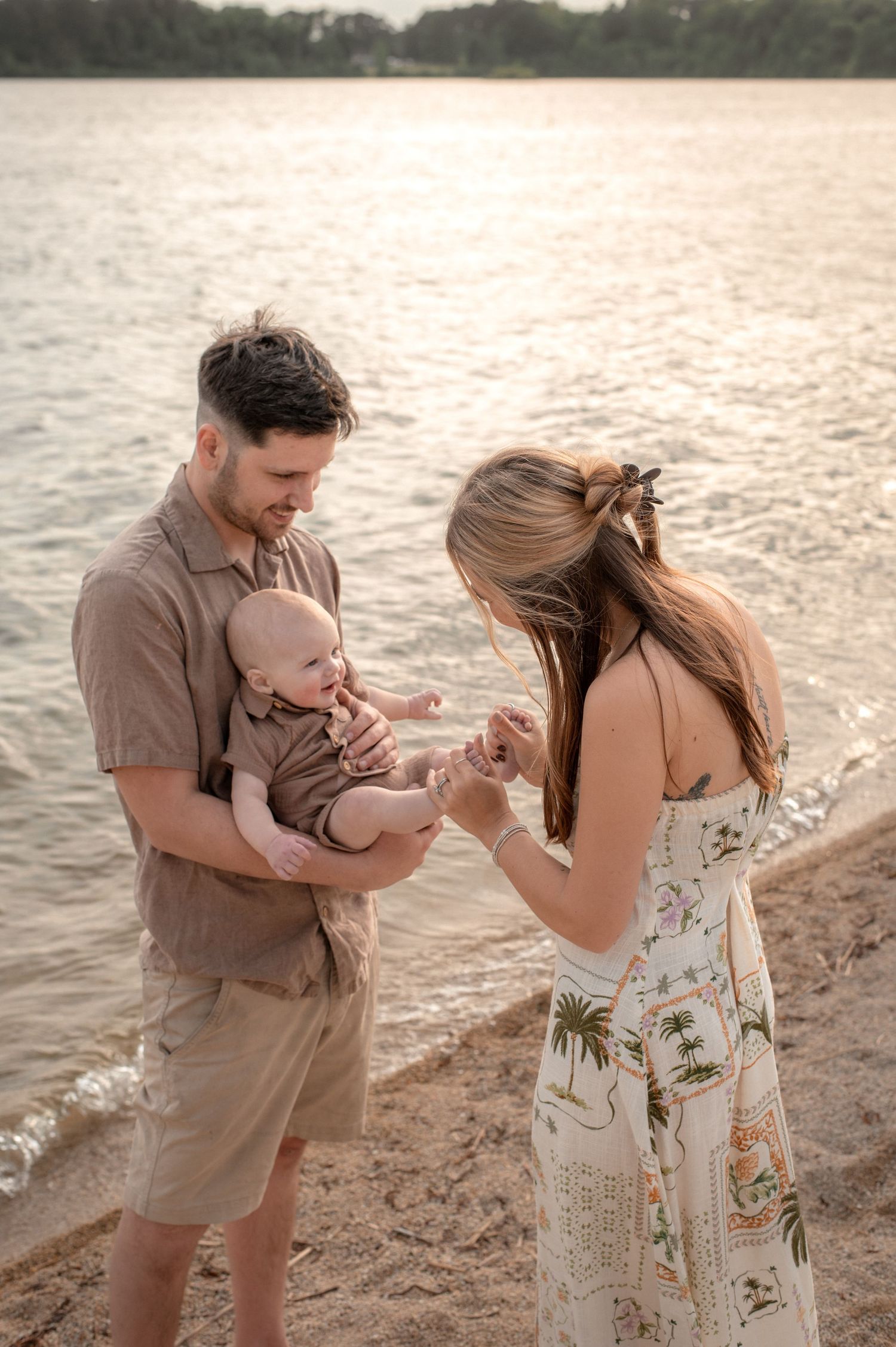 Young family with baby enjoying a golden sunset beach moment, parents lovingly interacting with their infant by the water.