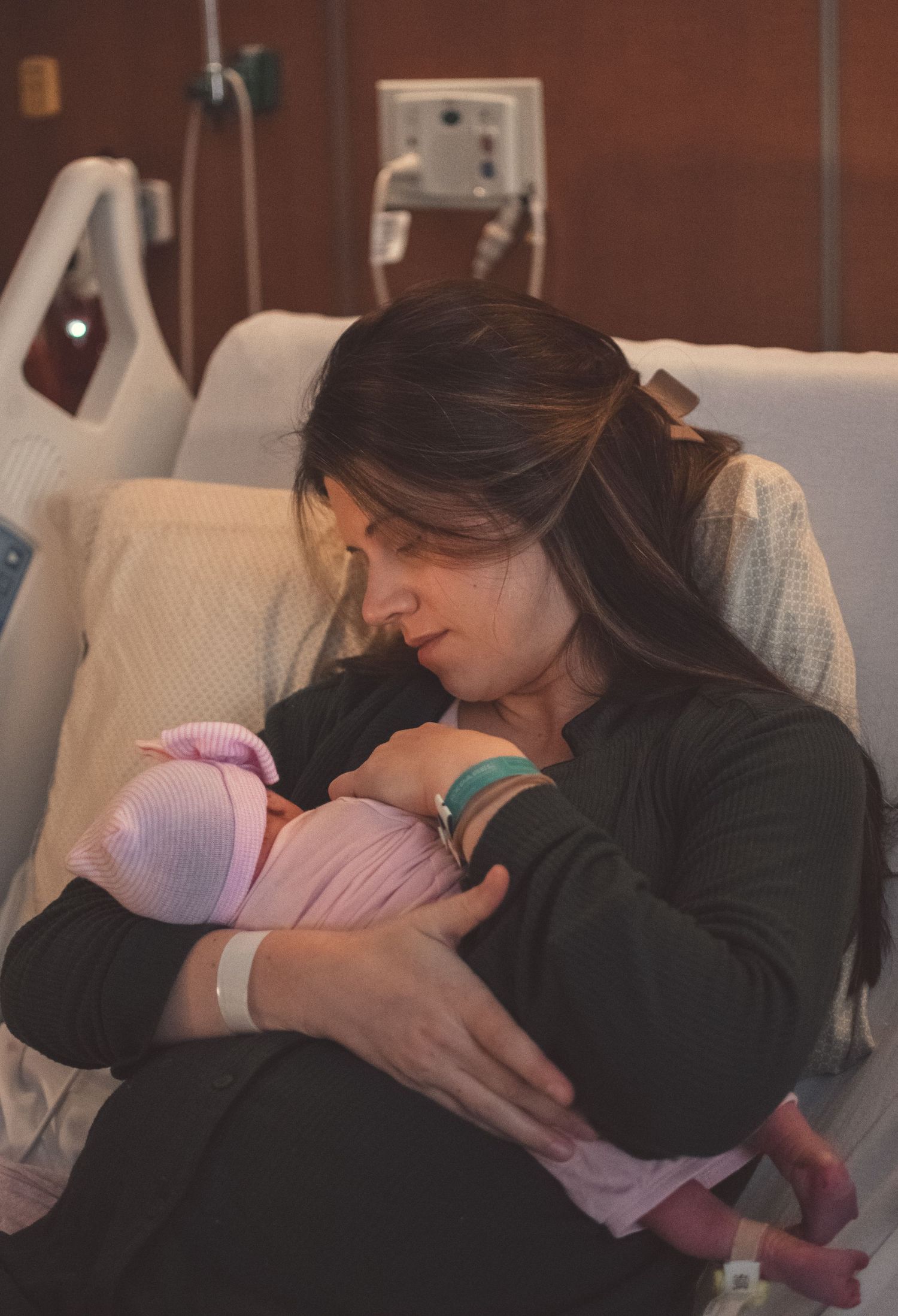 New mother in hospital bed tenderly holding and gazing at her swaddled newborn baby.