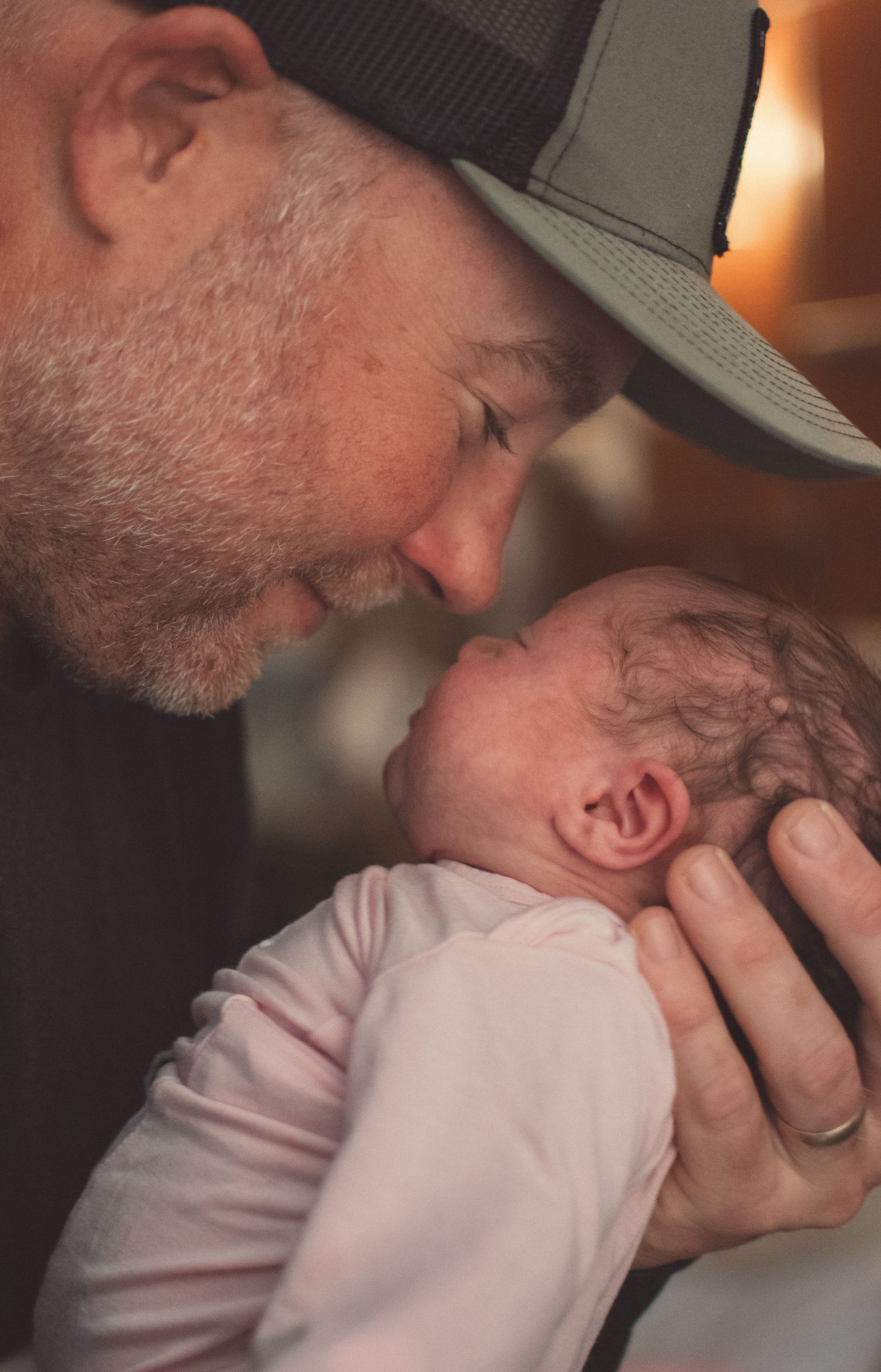 Loving father in trucker hat touching foreheads with his precious newborn baby girl.