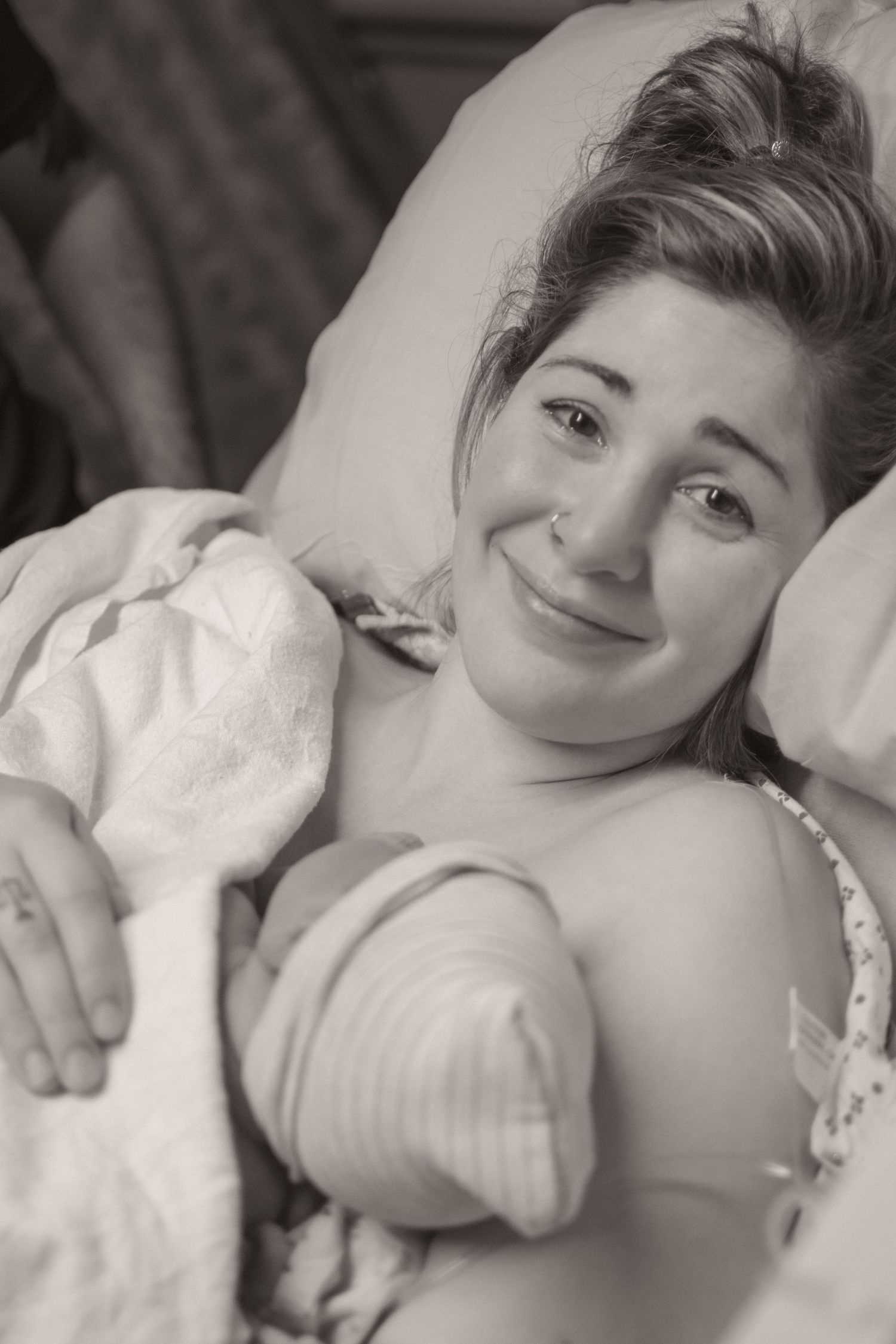 Black and white photo of a smiling new mother holding her newborn baby in a hospital bed after giving birth.