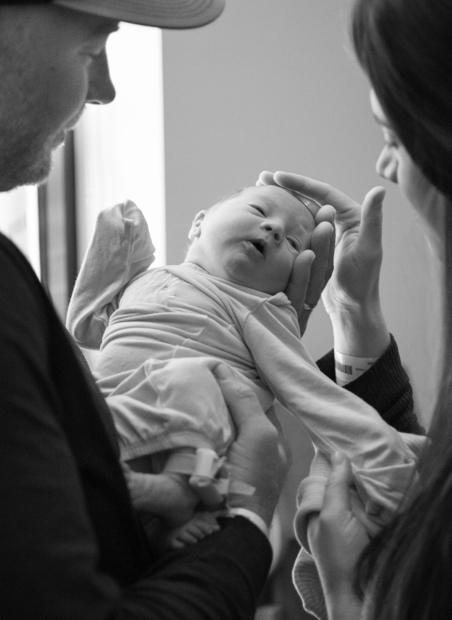 New parents lovingly cradle and stroke their newborn baby in a tender black and white photo.