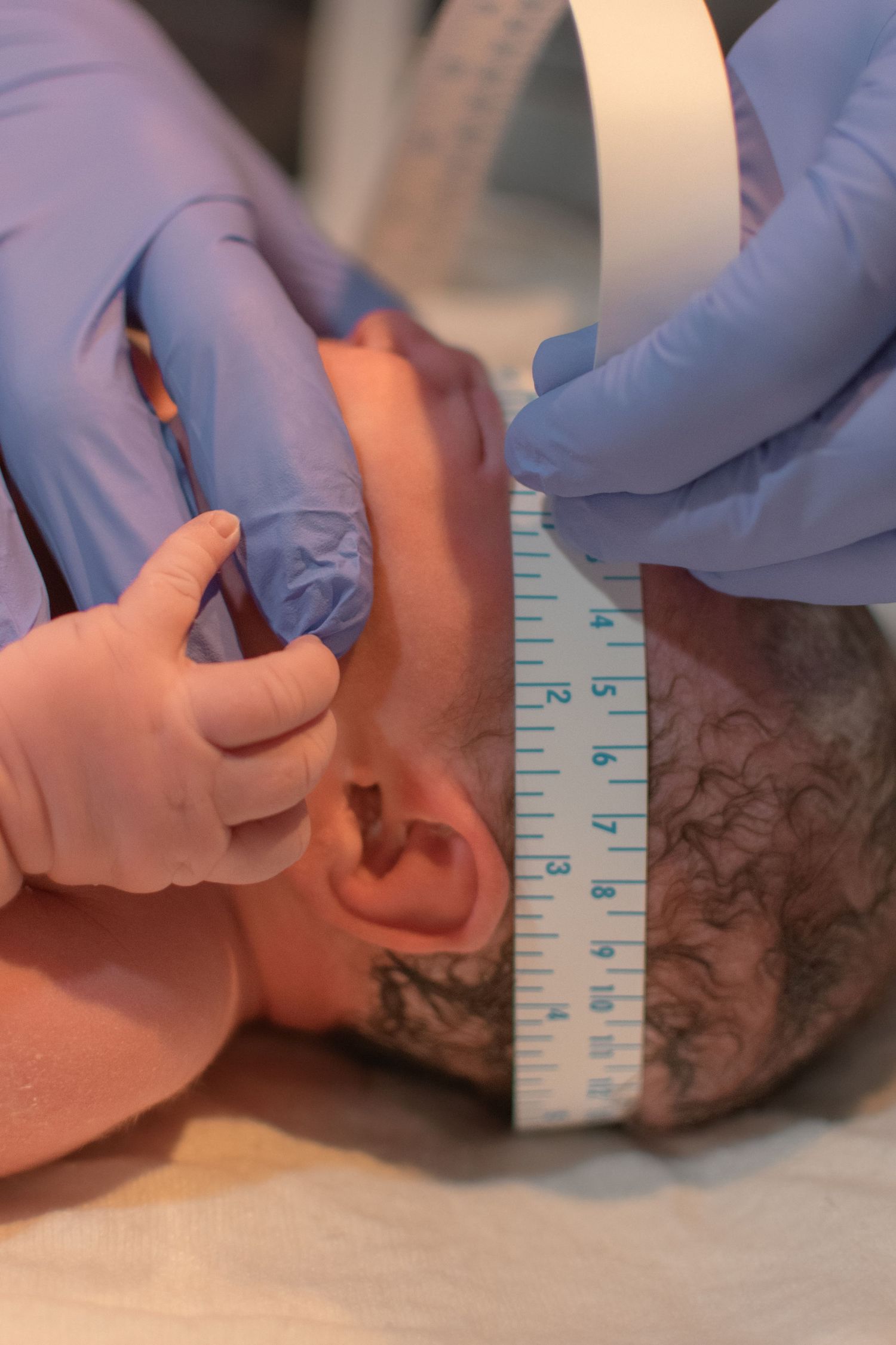 Medical professional in blue gloves measuring a newborn baby's head circumference with a tape measure.