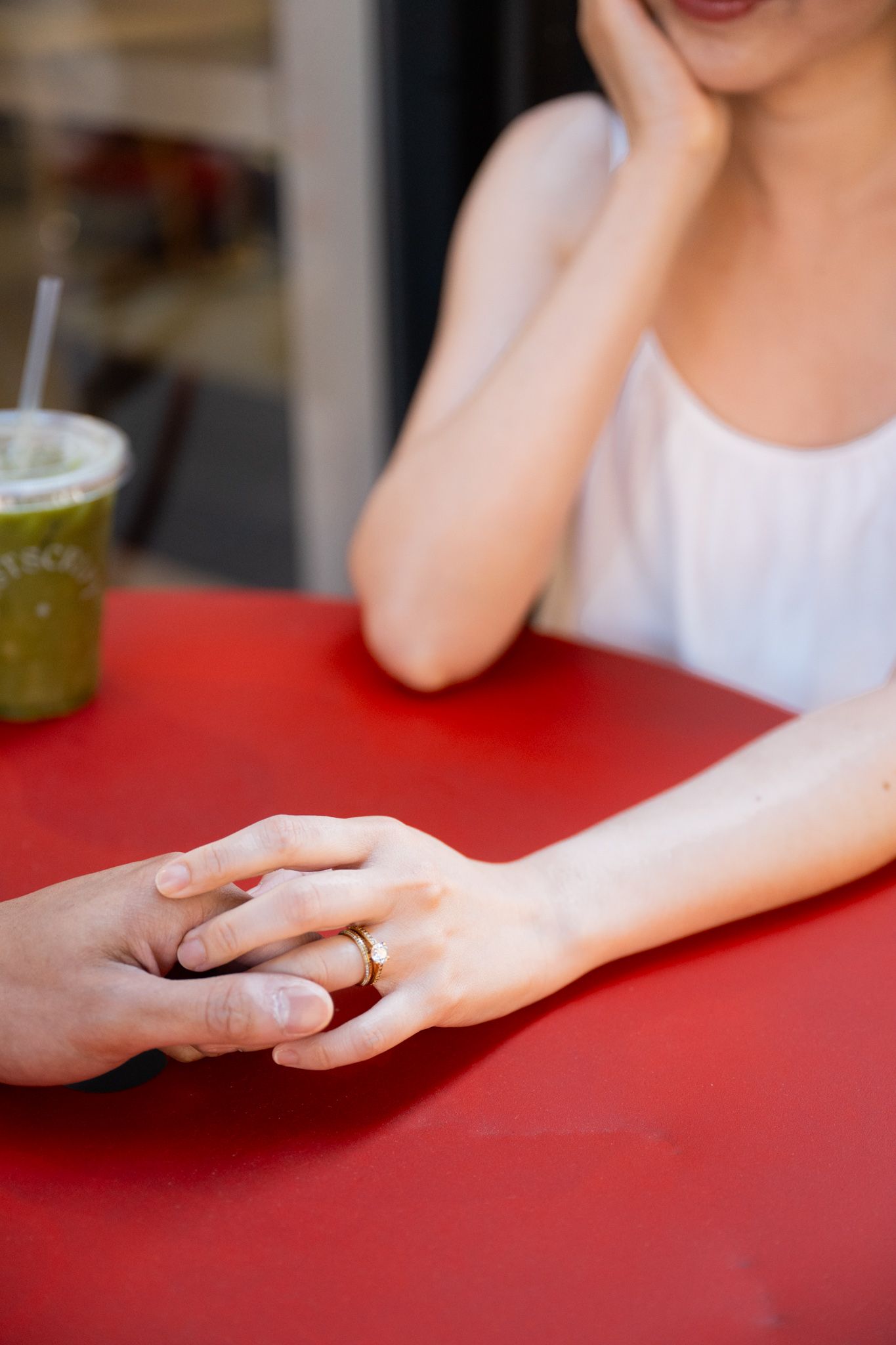 Two people holding hands on a red table, one wearing a gold ring, with a green iced drink nearby.