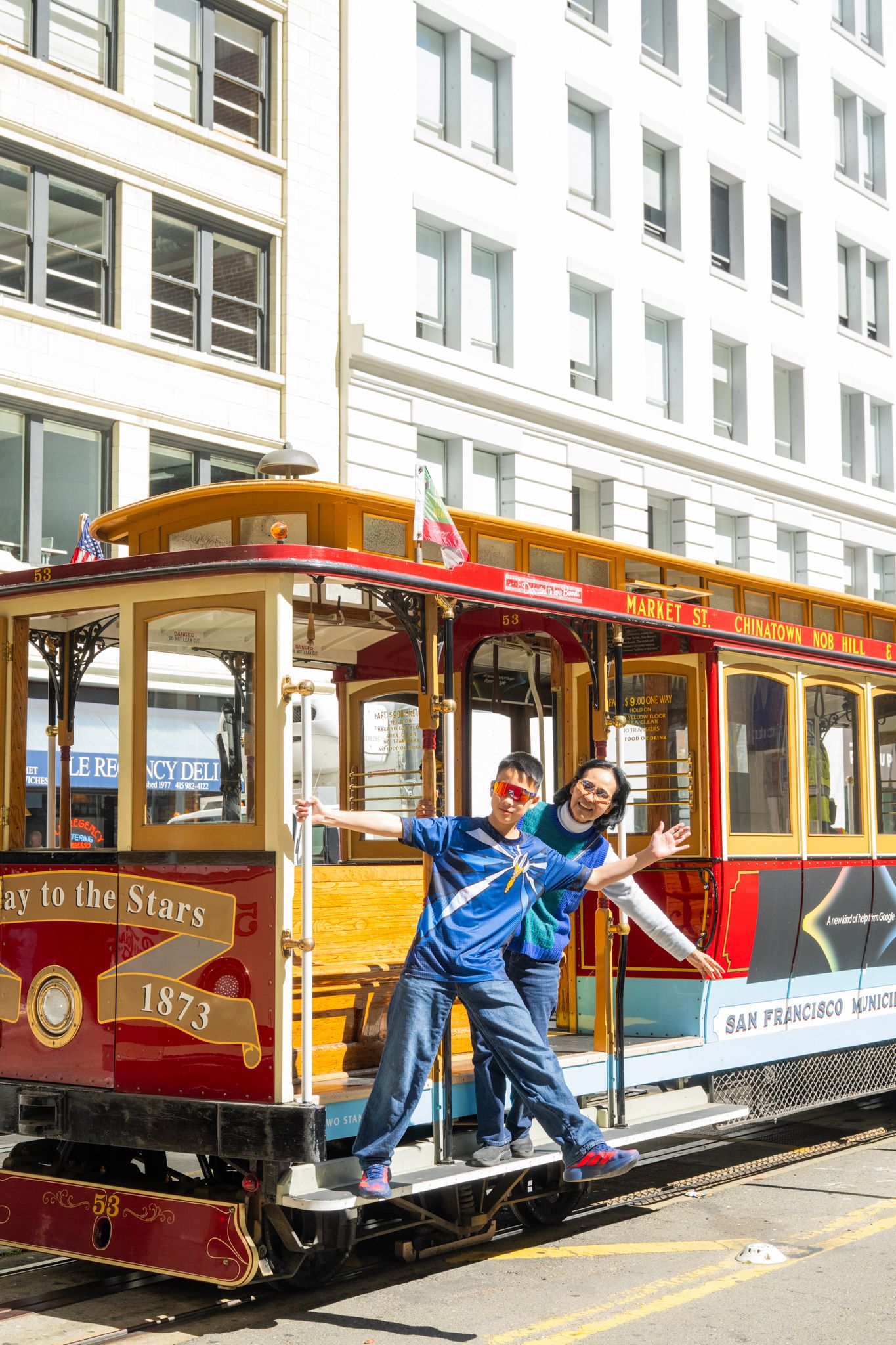 Two tourists pose on a classic San Francisco cable car number 1873 on a sunny day downtown.