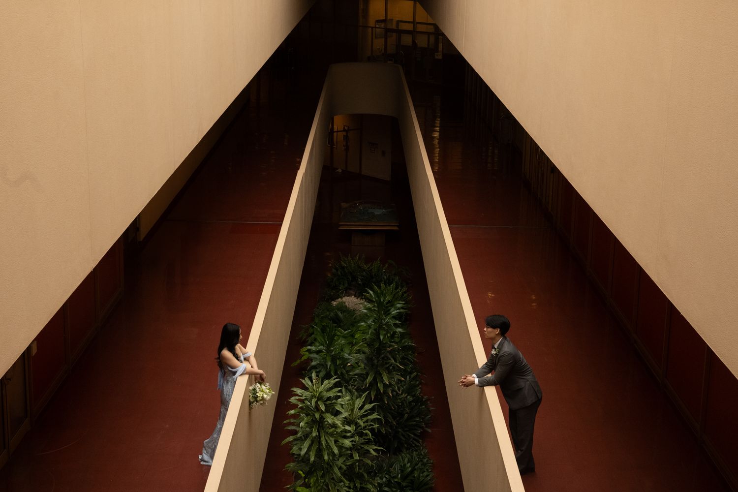 Bride and groom stand on opposite balconies of a building with lush green plants below.