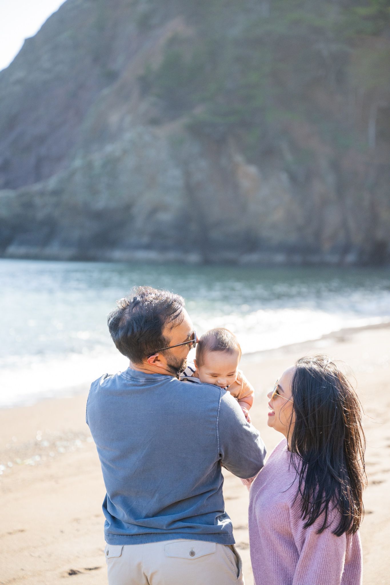 A loving family with parents and baby enjoy a sunny day together on a scenic rocky beach.