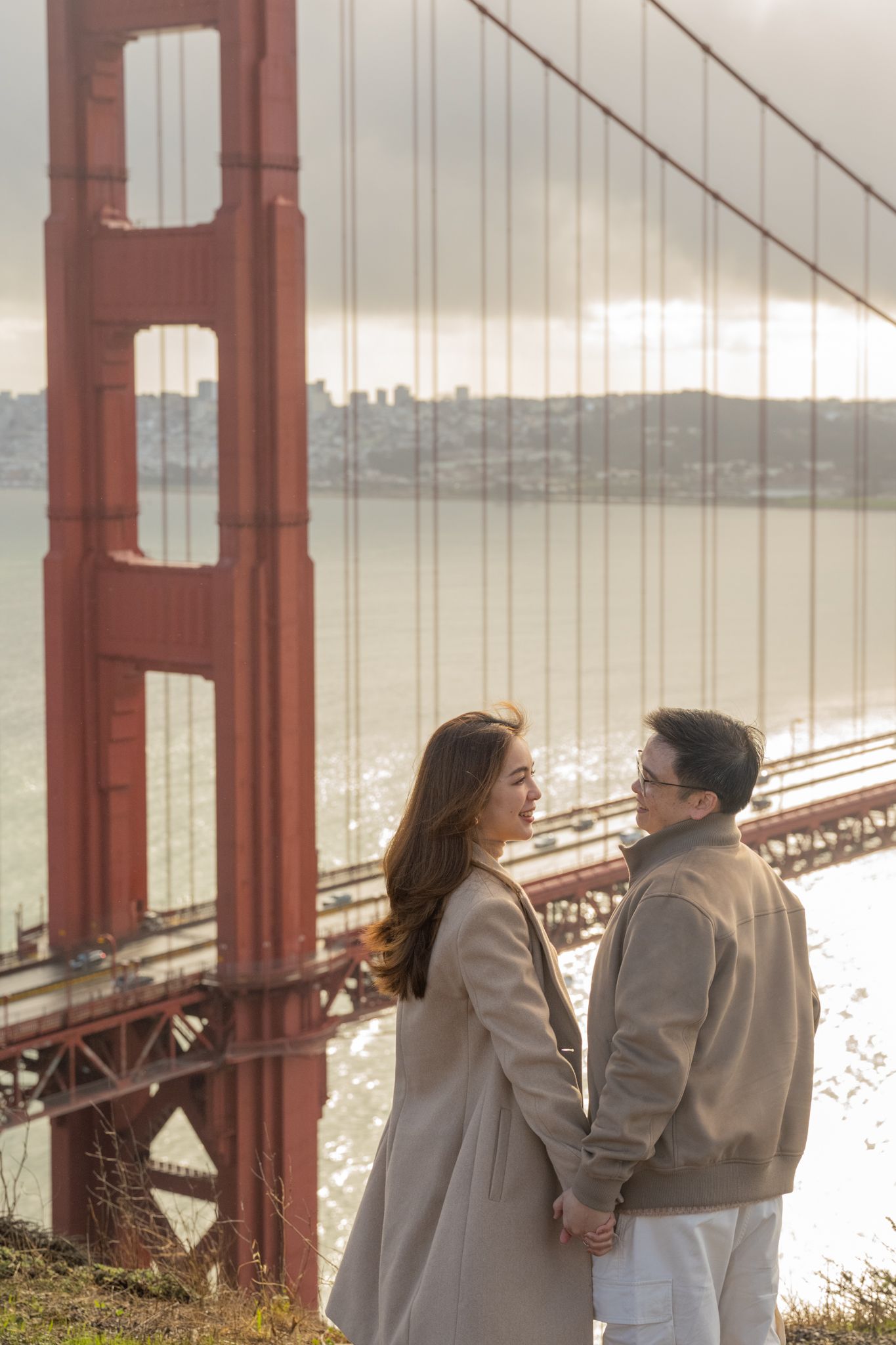 Couple holds hands facing each other with the iconic red Golden Gate Bridge and bay in the background.