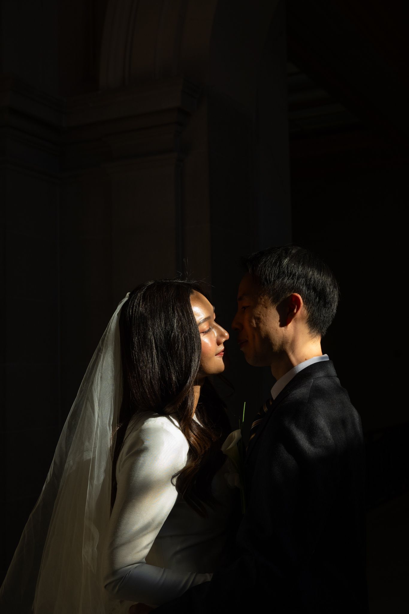 Bride and groom share an intimate moment in dramatic chiaroscuro lighting during their wedding ceremony.