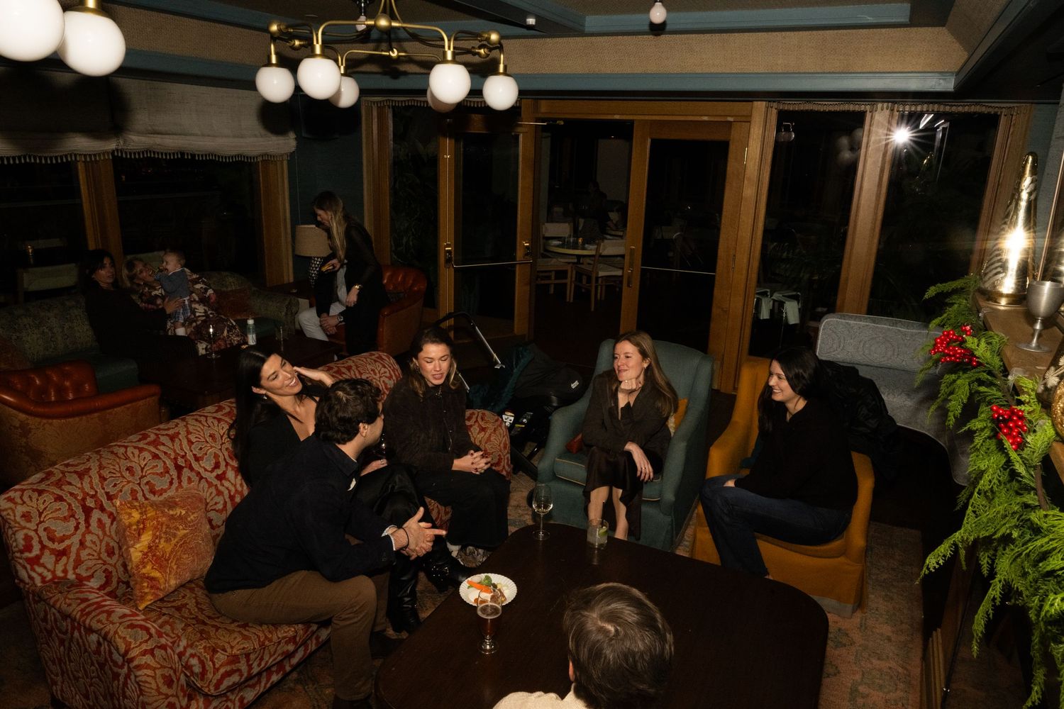 Guests relax on vintage sofas in a warmly lit lounge during an intimate evening gathering.