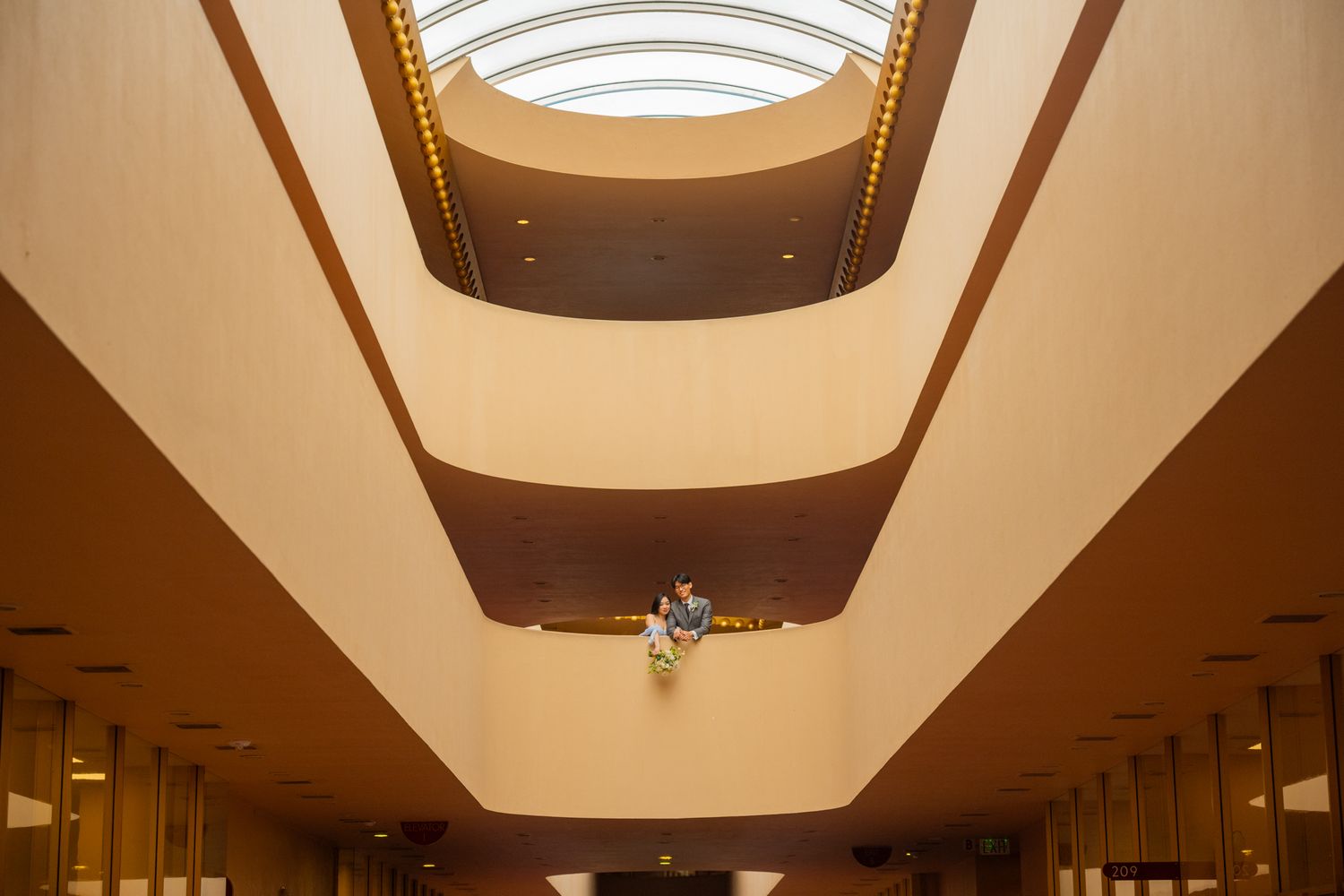 Wedding couple stands beneath a stunning multi-tiered skylight in an elegant building atrium.