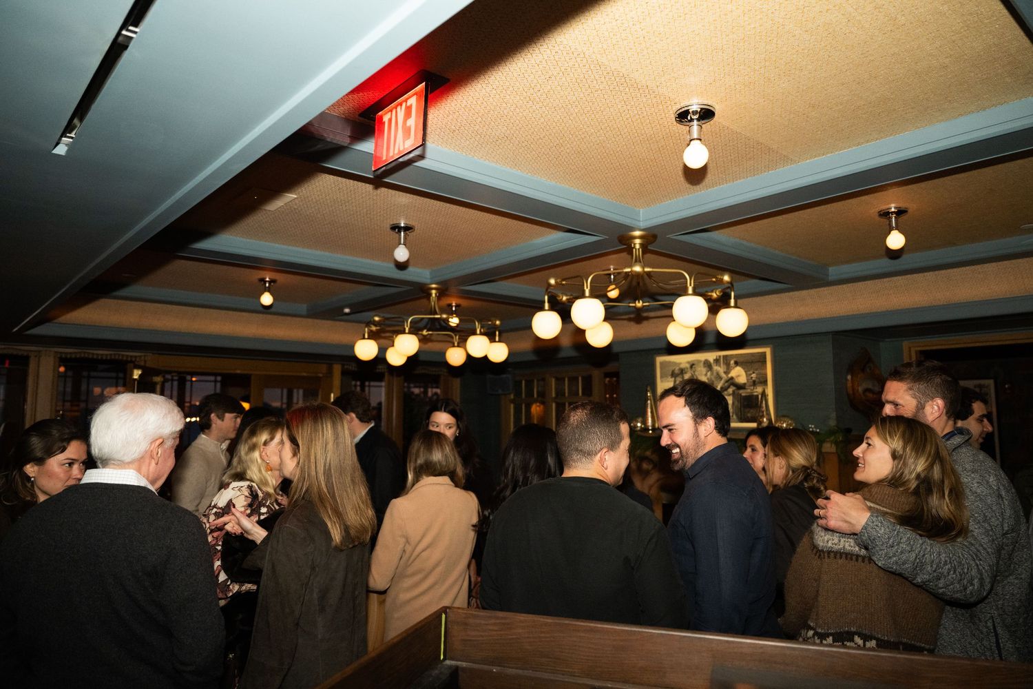 Wedding reception guests mingle in a warmly lit restaurant venue with globe pendant lighting.