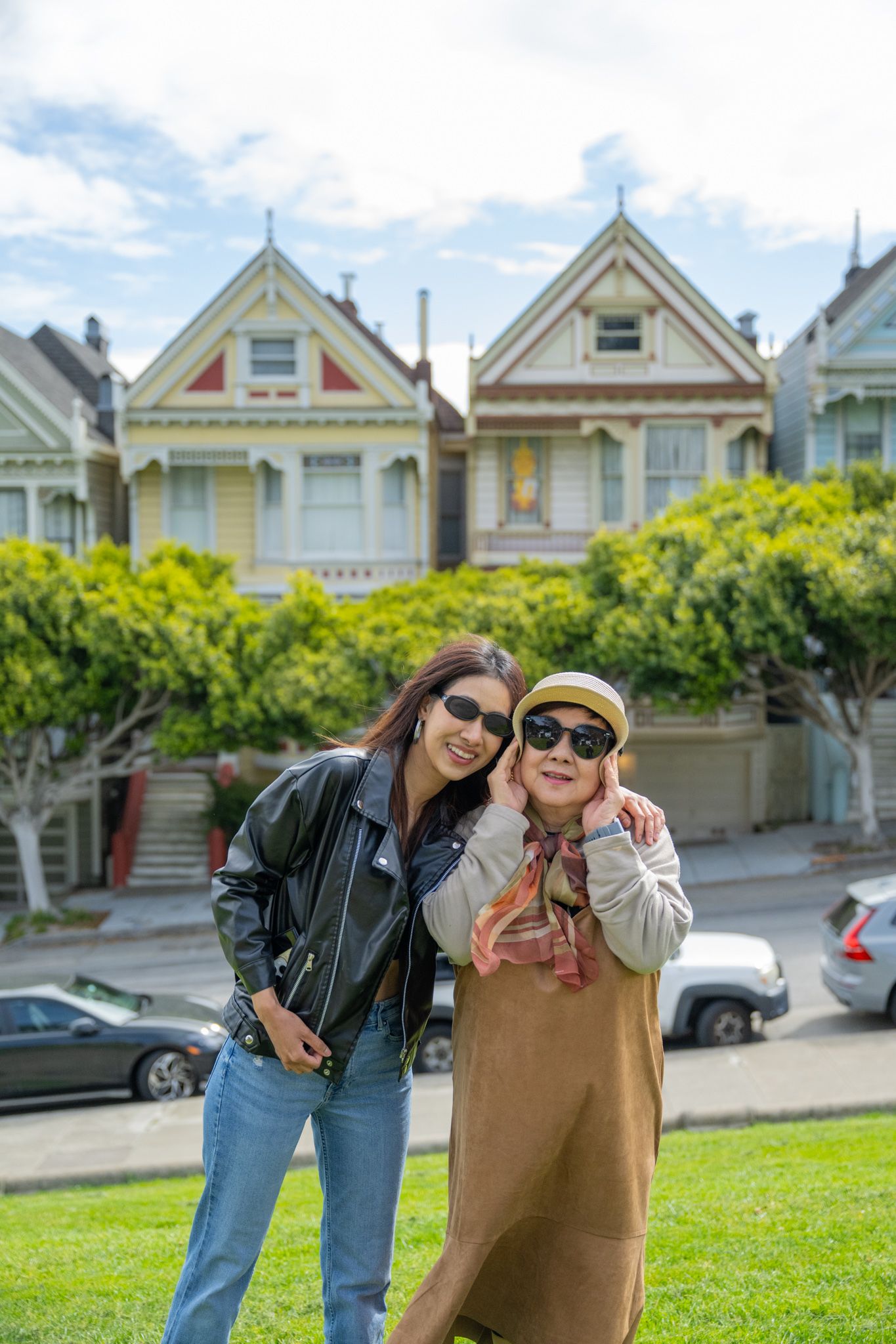 Two smiling Asian women pose together in front of San Francisco Painted Ladies Victorian houses.