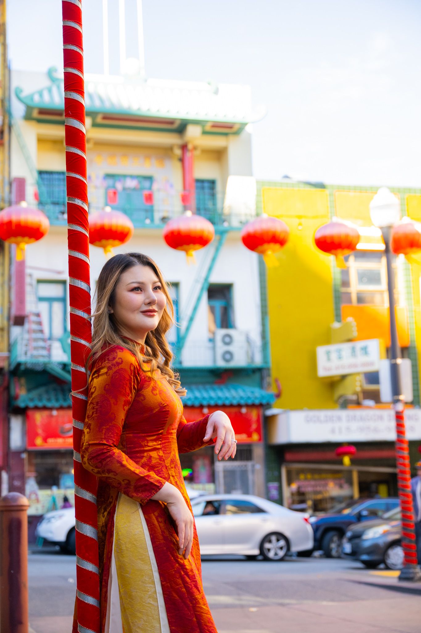 Woman in traditional red Vietnamese ao dai dress poses in San Francisco Chinatown with red lanterns.
