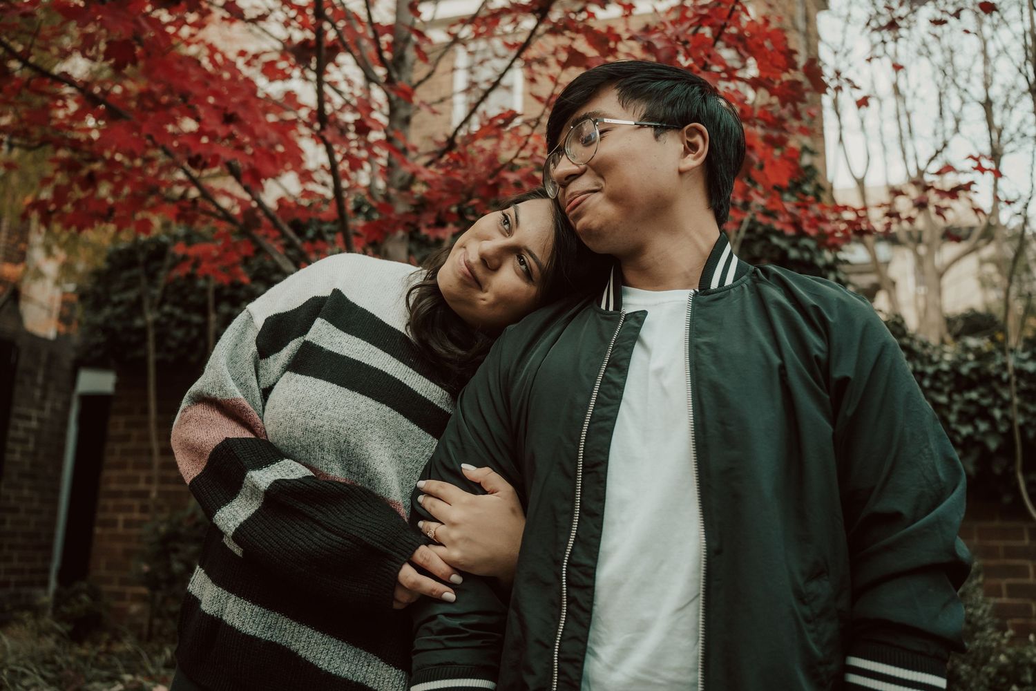 A couple in dark clothing embraces tenderly against a backdrop of autumn foliage and brick walls in Old town Alexandria