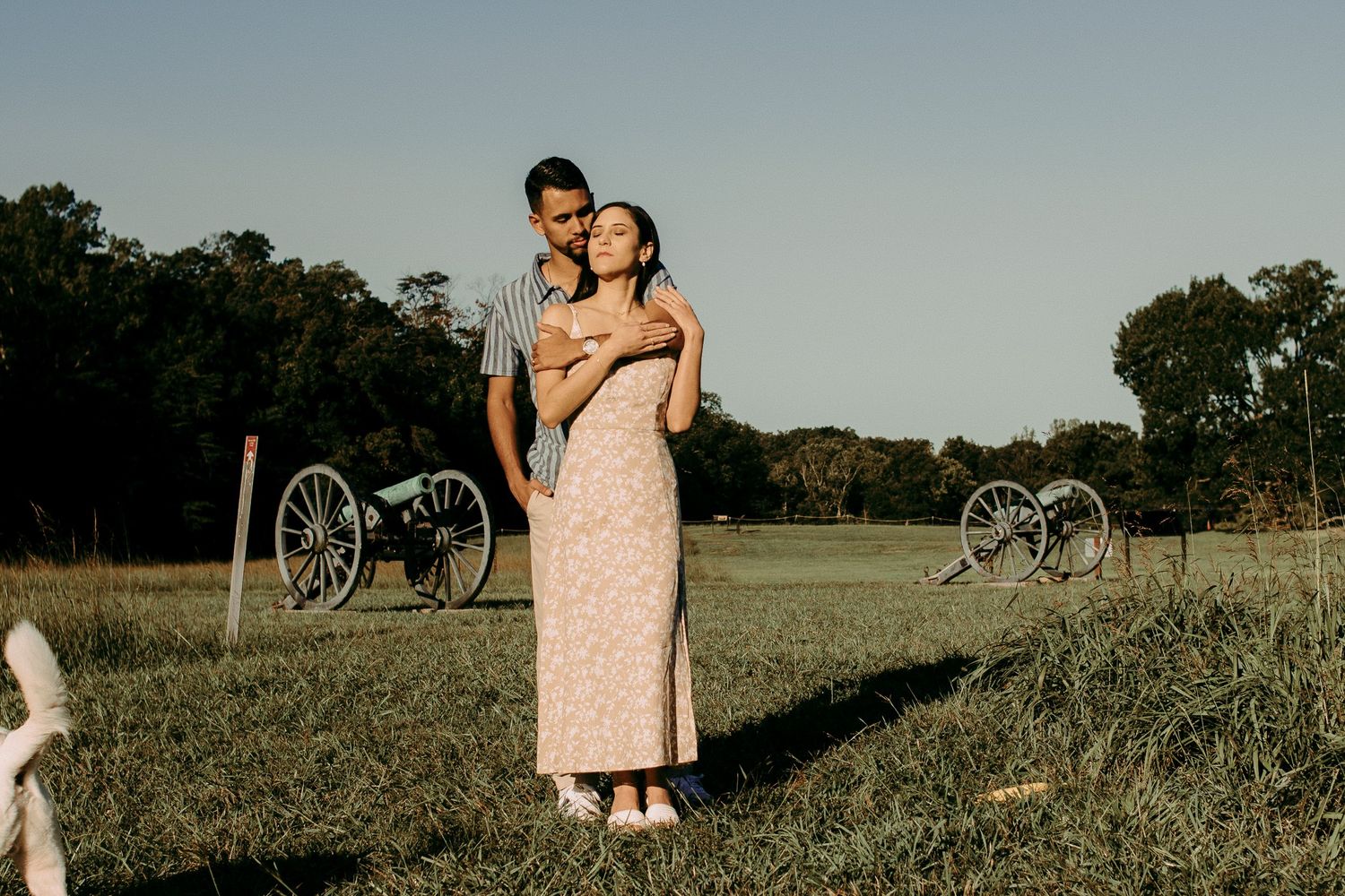 Couple embraces in a sunlit field during a romantic outdoor photoshoot.