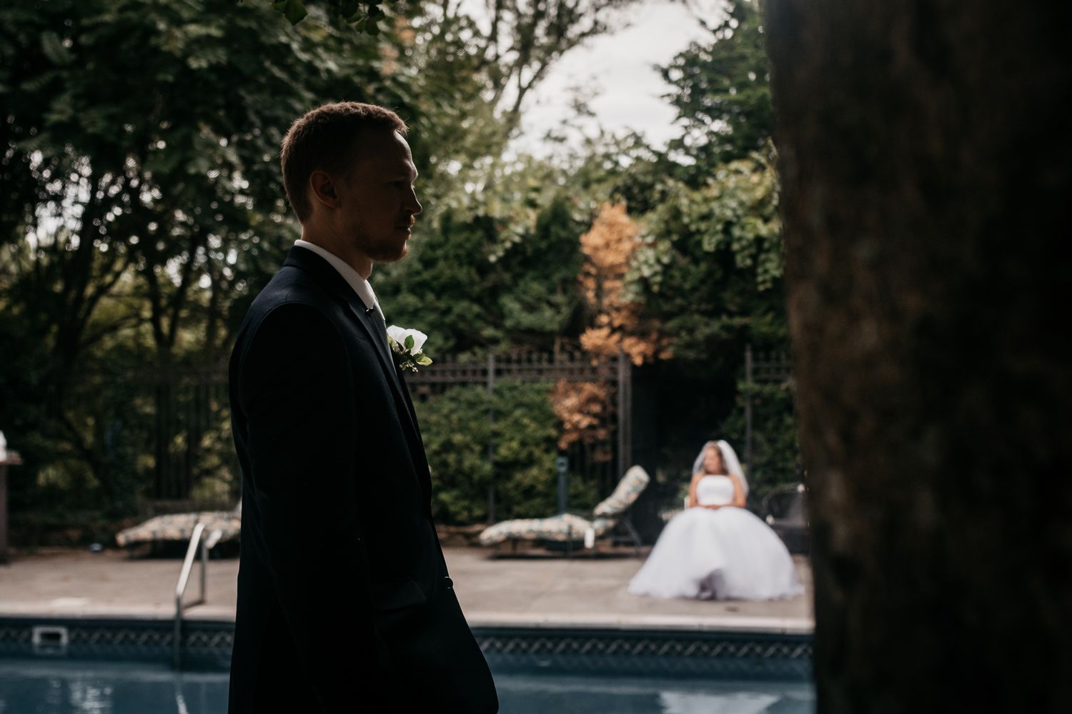 A couple in wedding attire walks together through a lush garden setting during an autumn day.