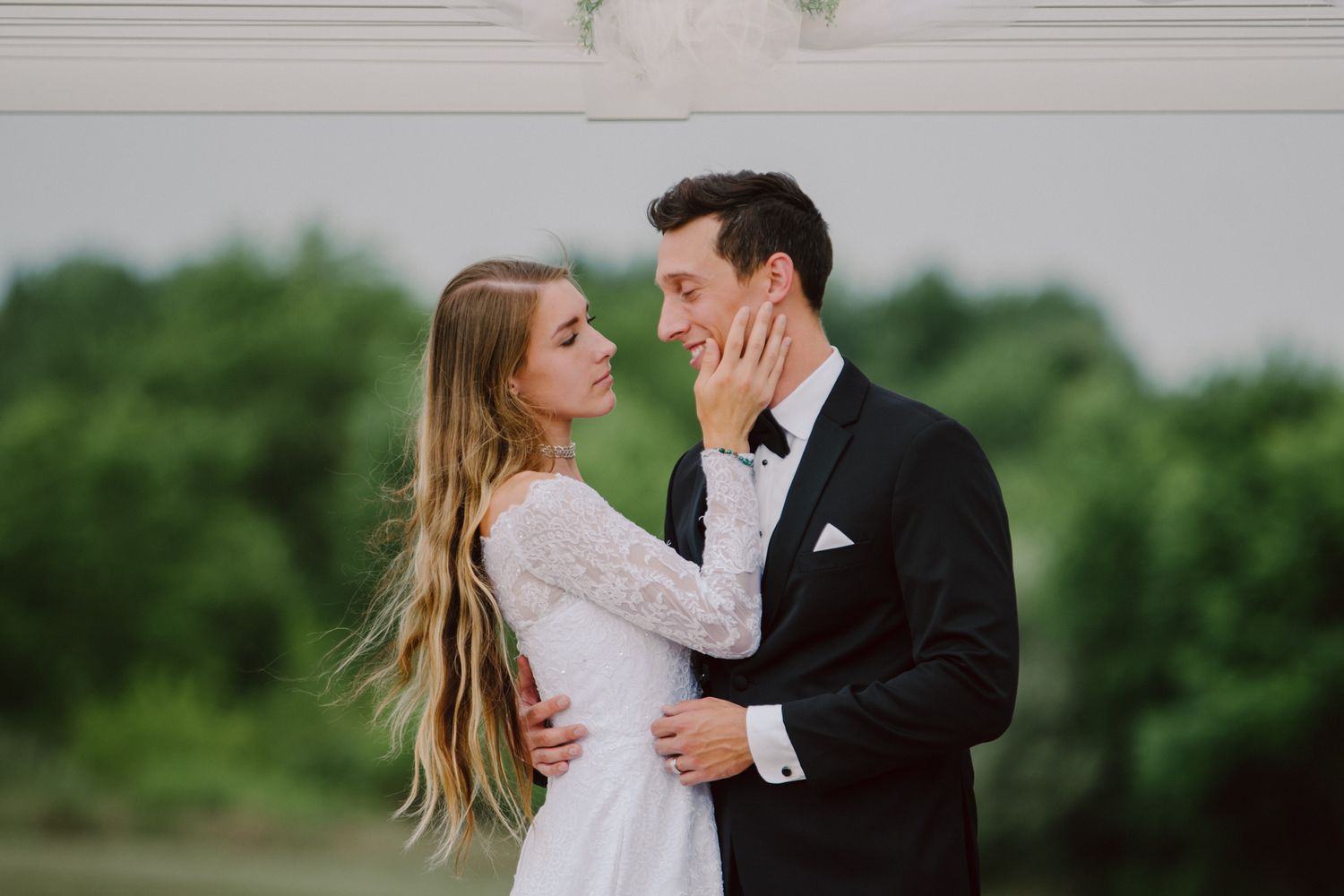 A couple in wedding attire shares an intimate moment in a garden setting with lush greenery in the background.