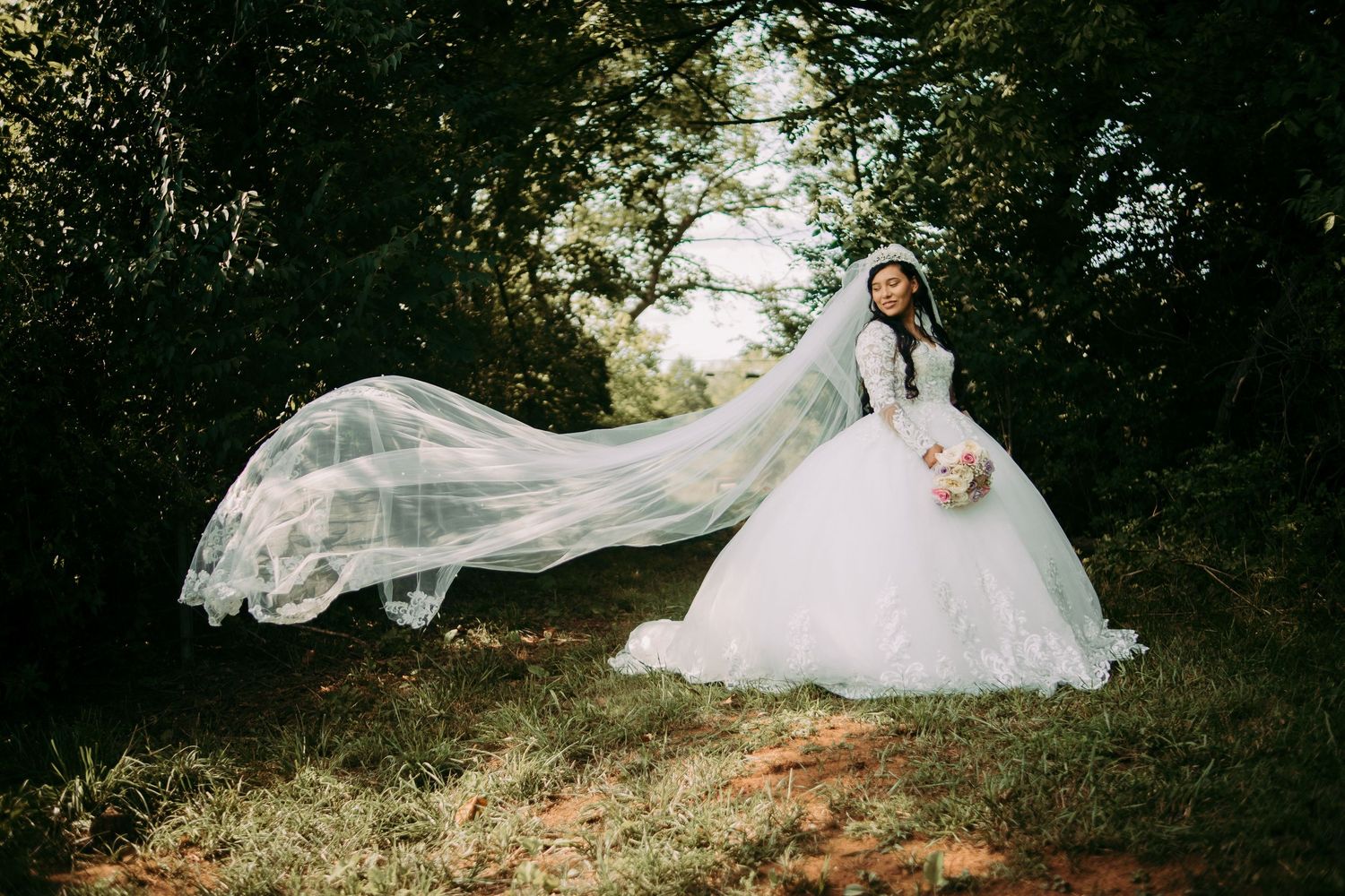 A bride in a flowing white wedding dress poses gracefully on a grassy hill during a romantic outdoor photo session.