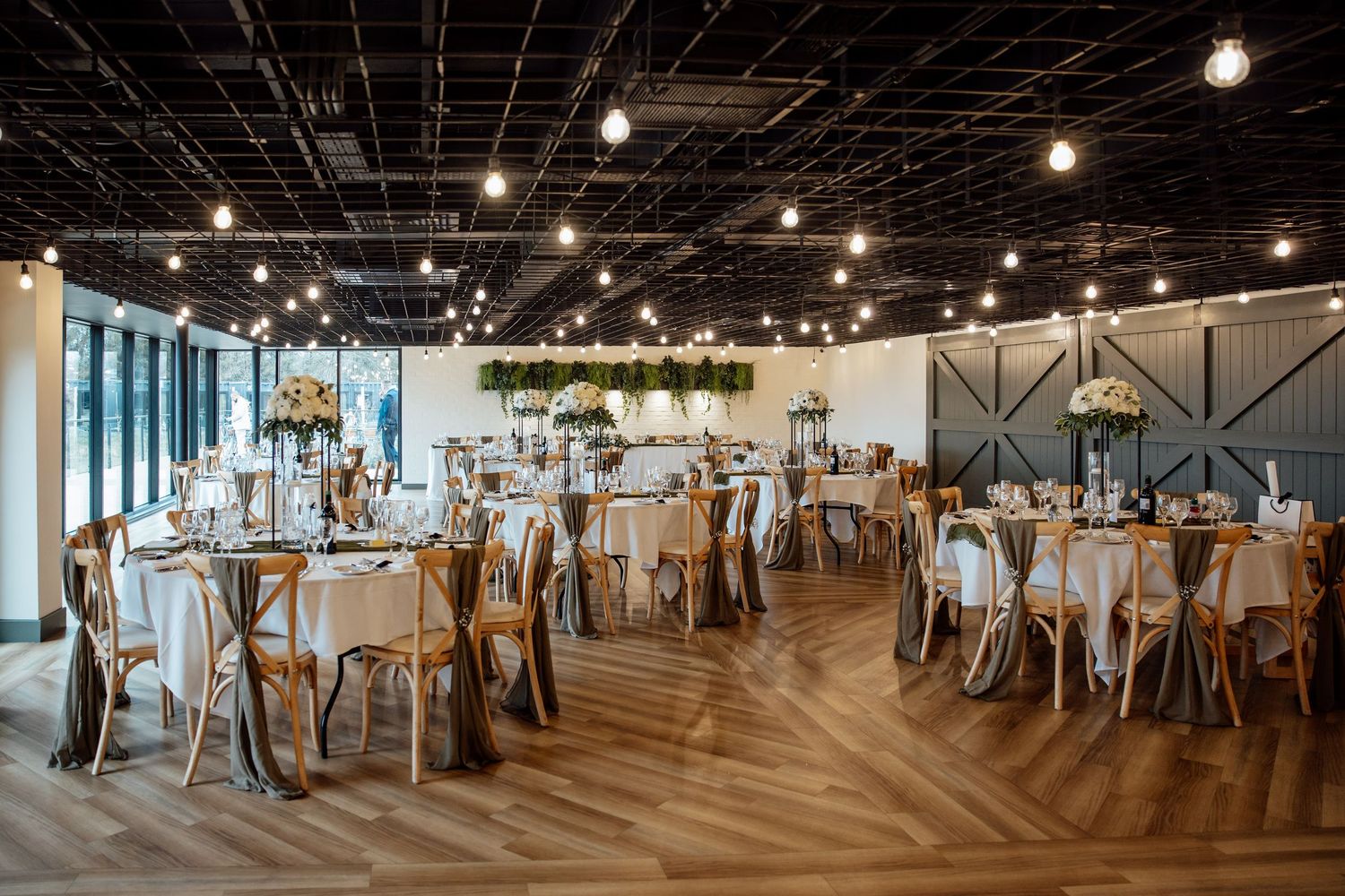 Elegant wedding reception venue with string lights, round tables, and hardwood floors.